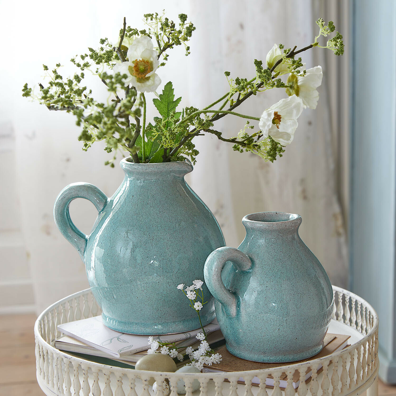 Due brocche in ceramica turchese con manici su tavolo metallico bianco con fiori e libri