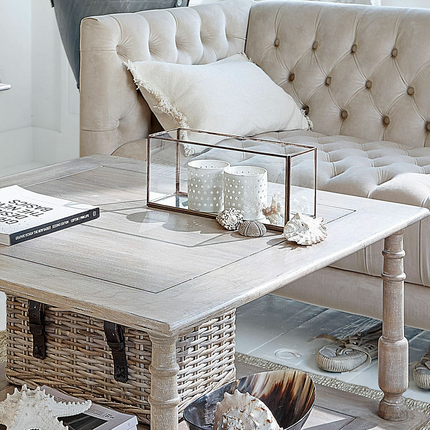 Portacandele Flavin Tavolino in legno chiaro con cesto in vimini e decorazioni davanti a divano beige capitonné