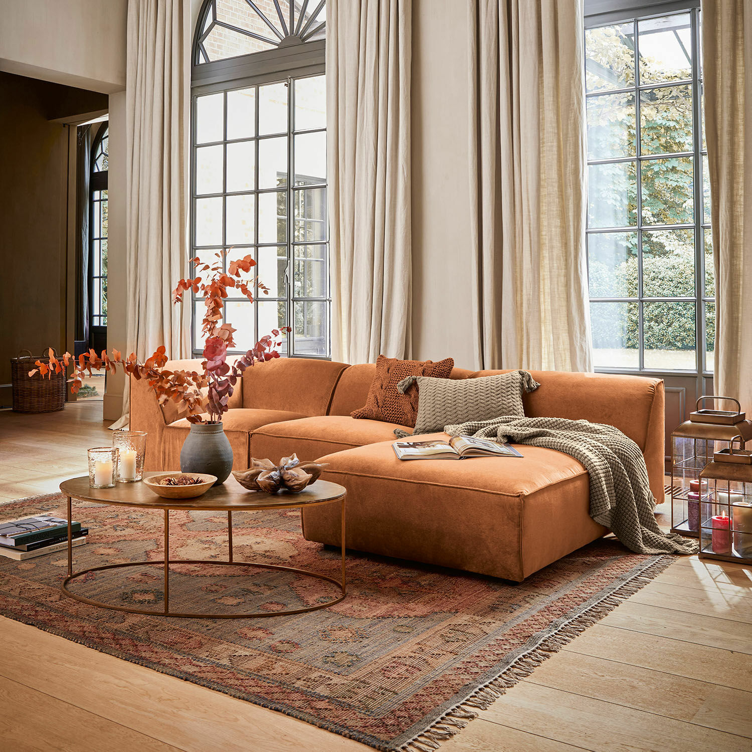 Divano McLean Divano angolare color mattone con cuscini e coperta in soggiorno luminoso con grandi finestre