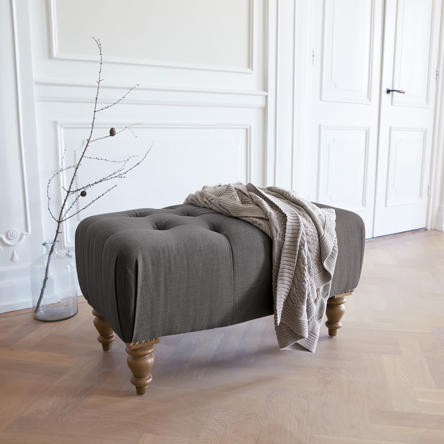 Pouf Durance Pouf imbottito grigio con gambe in legno e coperta beige in interno luminoso