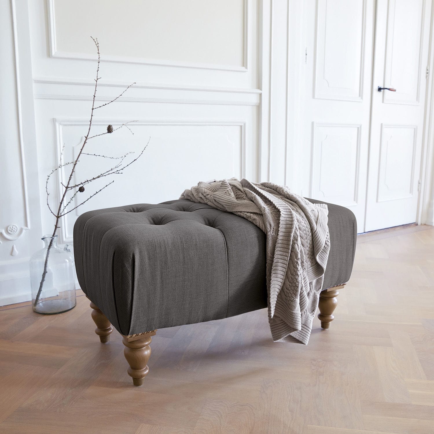 Pouf Durance Pouf imbottito grigio con gambe in legno e coperta beige in interno luminoso
