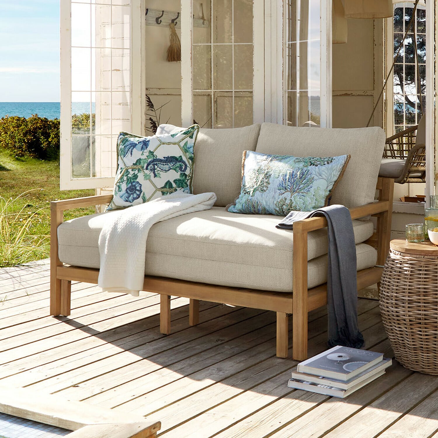 Divano letto Tjorna Divano beige chiaro con struttura in legno su terrazza con vista su giardino e mare