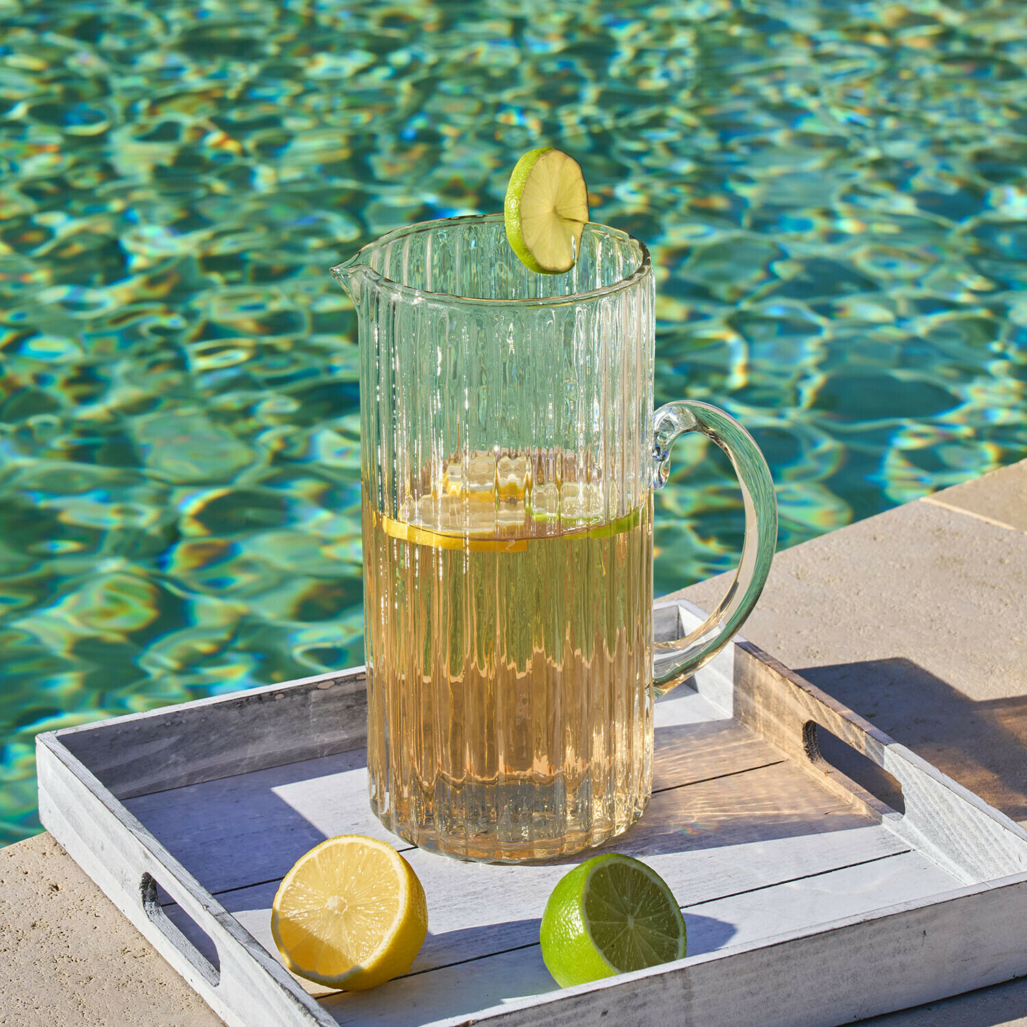 Caraffa Solerón Caraffa di vetro trasparente con bevanda e fetta di lime su vassoio bianco vicino alla piscina