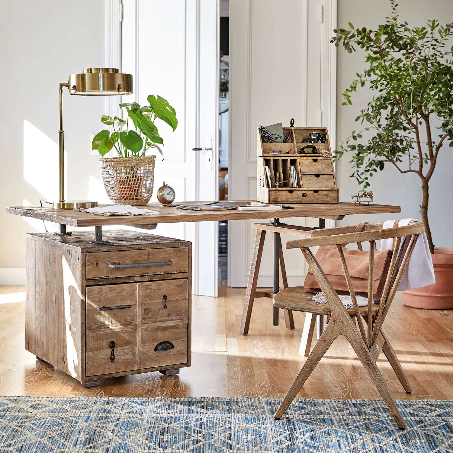 Scrivania in legno con cassetti e maniglie in metallo, lampada dorata e pianta in cesta intrecciata