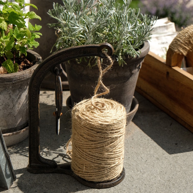 Spola di corda di juta naturale su supporto metallico accanto a vasi di erbe per giardinaggio