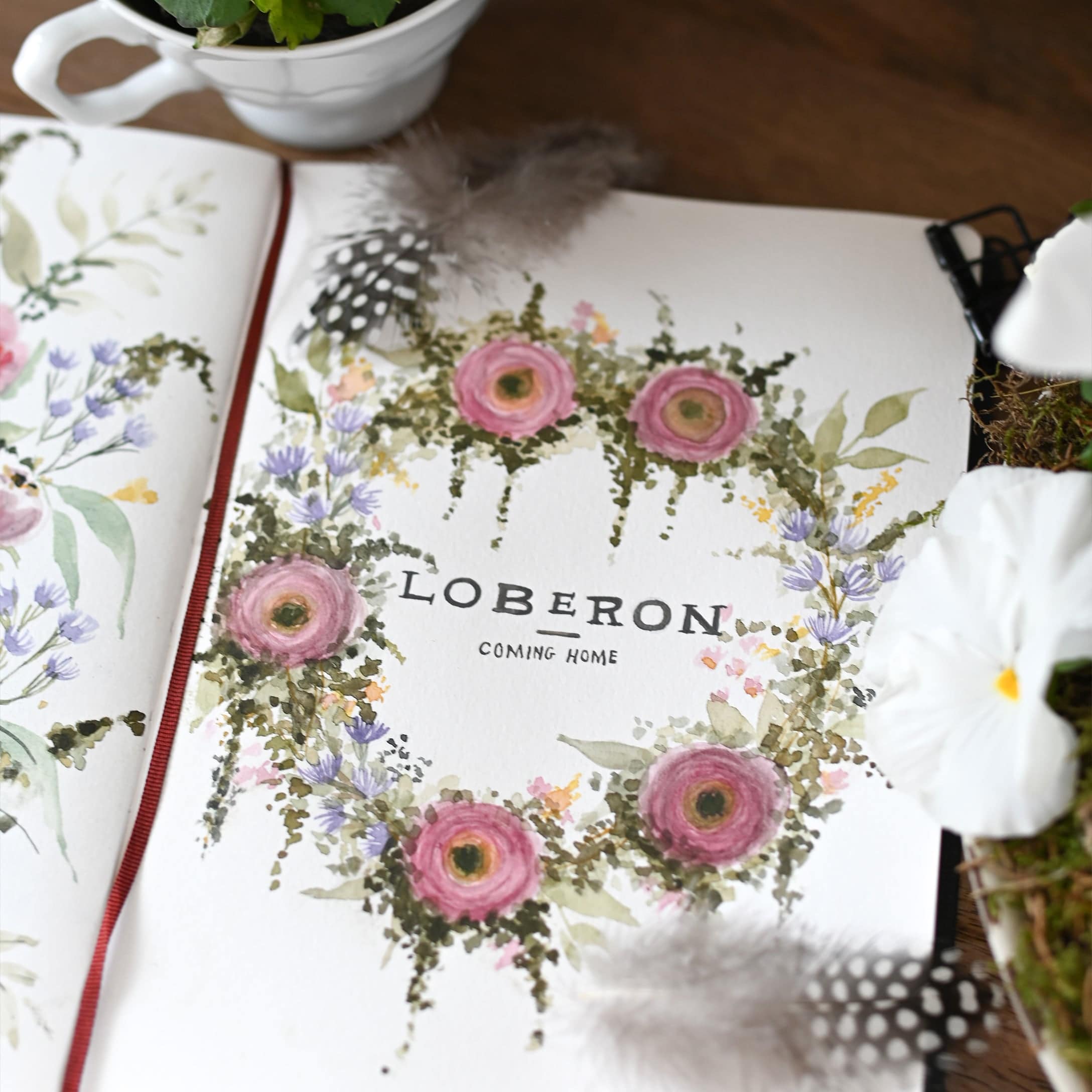 Corona floreale ad acquerello con fiori rosa e viola, piume e fiori bianchi su carta