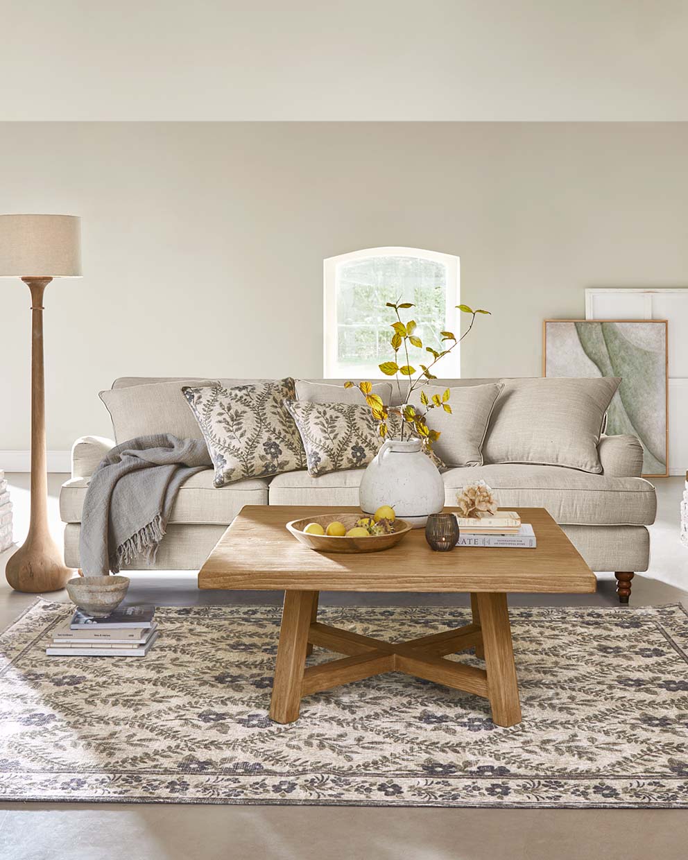 Divano beige con cuscini e tavolino in legno su tappeto decorato in soggiorno luminoso