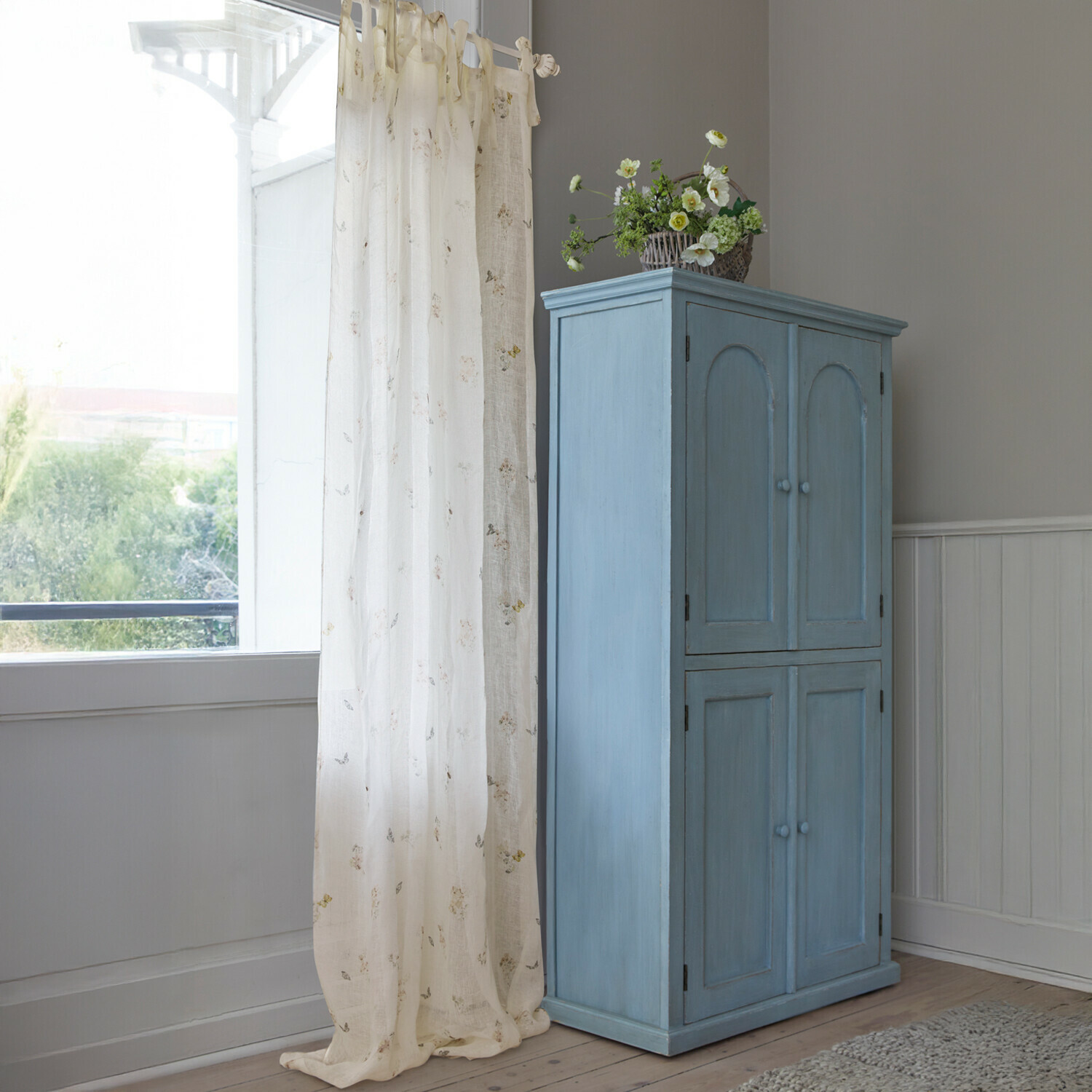 Tenda Salénaïs Armadio in legno blu con quattro ante e cesto di fiori decorativo in stanza luminosa