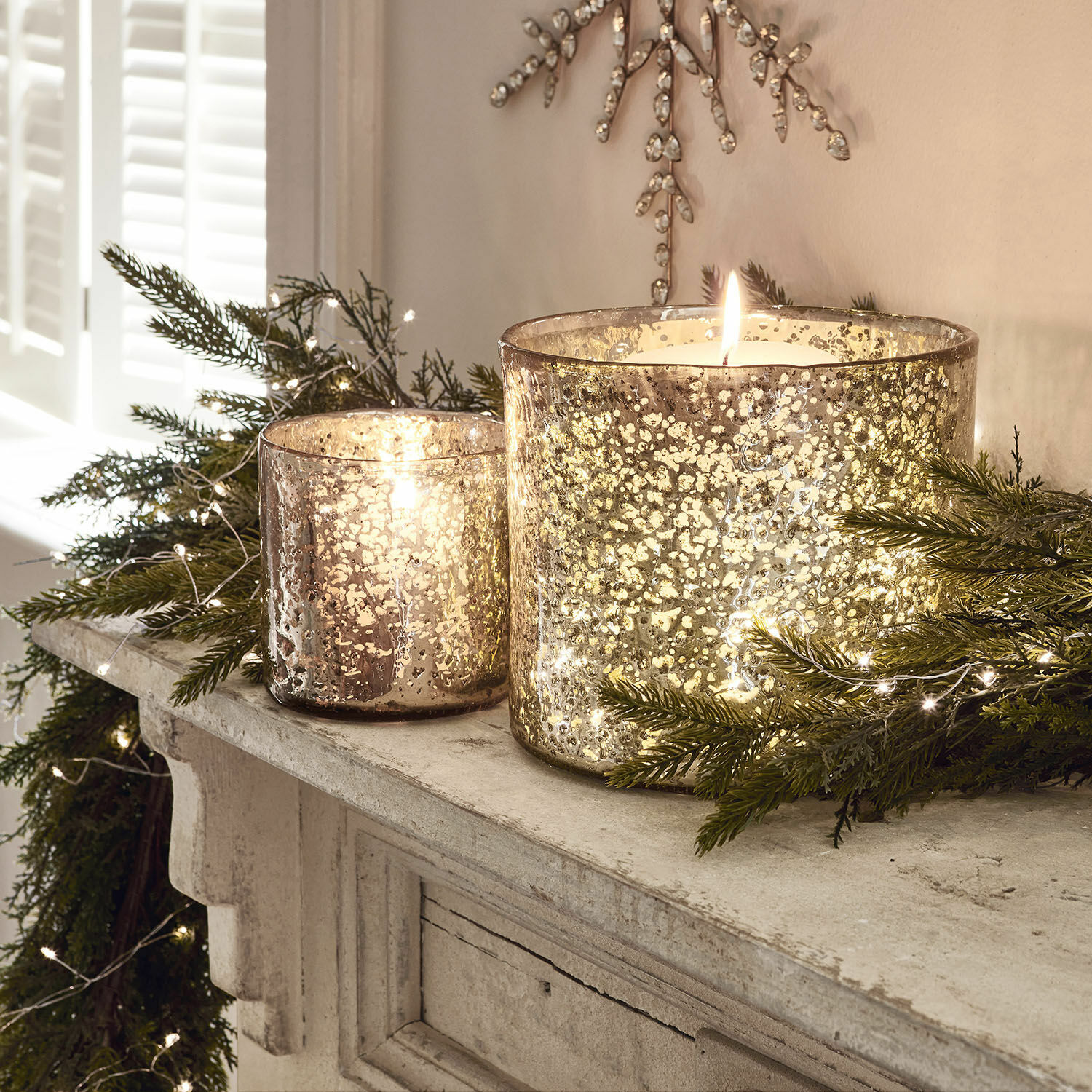 Coppia di portacandele Samuel Due portacandele in vetro con effetto argento invecchiato su camino con rami verdi e luci decorative