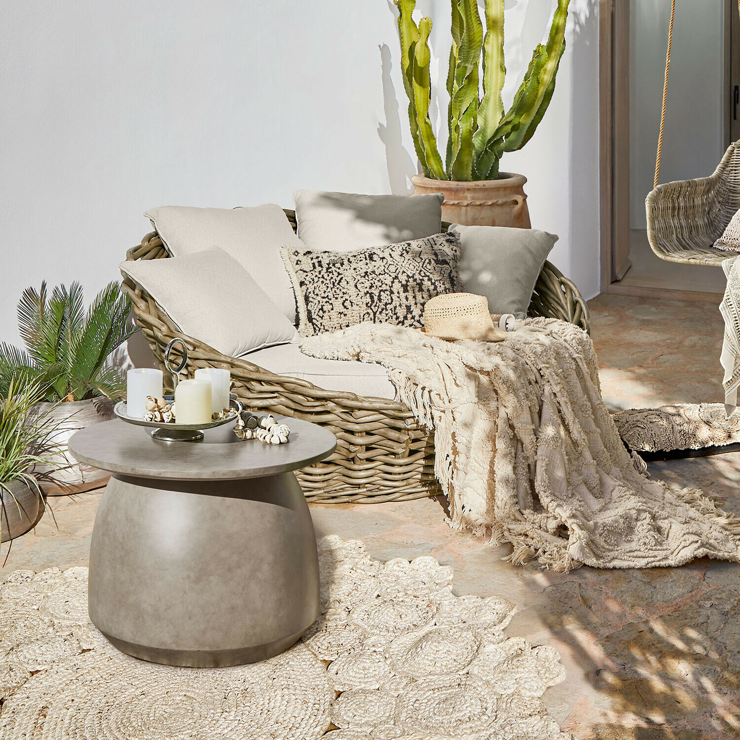 Divano rotondo in rattan con cuscini crema e coperta su terrazza con tavolino in cemento