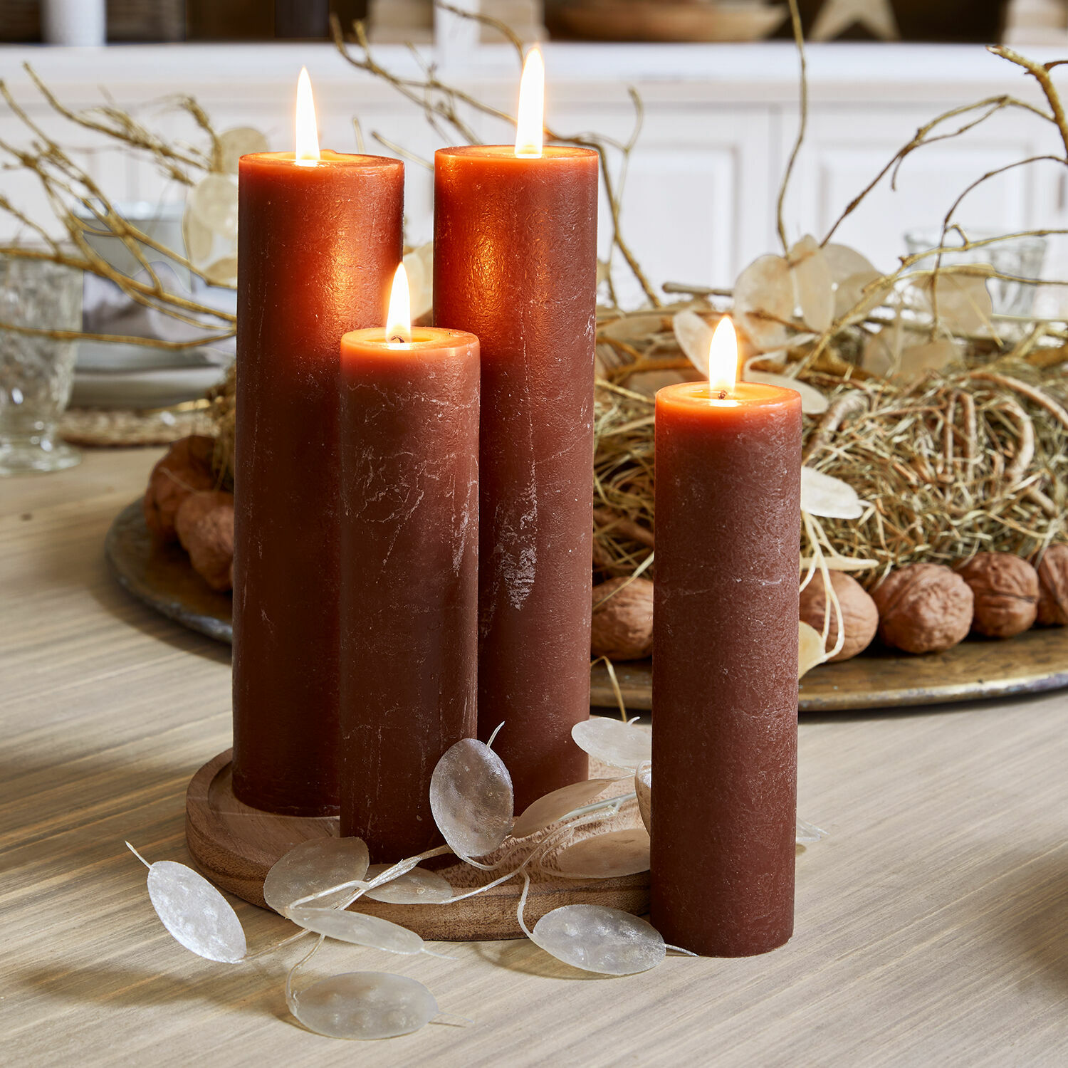 Set di 4 candele Avinal Quattro candele di cera marrone accese su base in legno con decorazioni sul tavolo