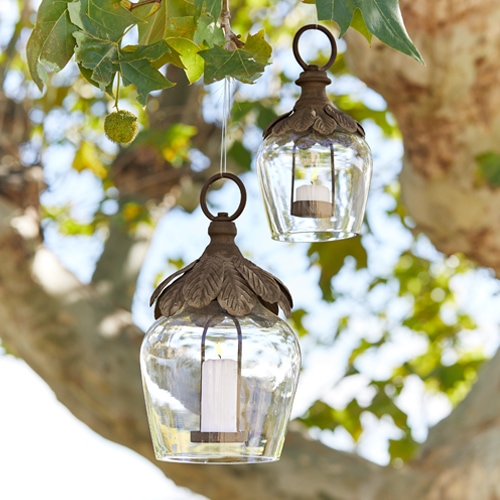 Lanterna in vetro appesa a un albero con decorazioni in metallo e candele bianche per decorazione da giardino
