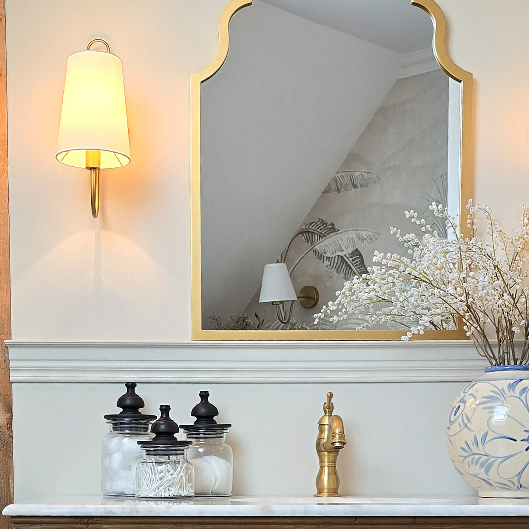 Specchio dorato con cornice decorativa sopra lavabo in marmo con rubinetto in ottone e barattoli di vetro