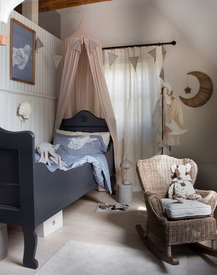 Camera per bambini accogliente con letto in legno nero e sedia a dondolo in vimini dai toni naturali