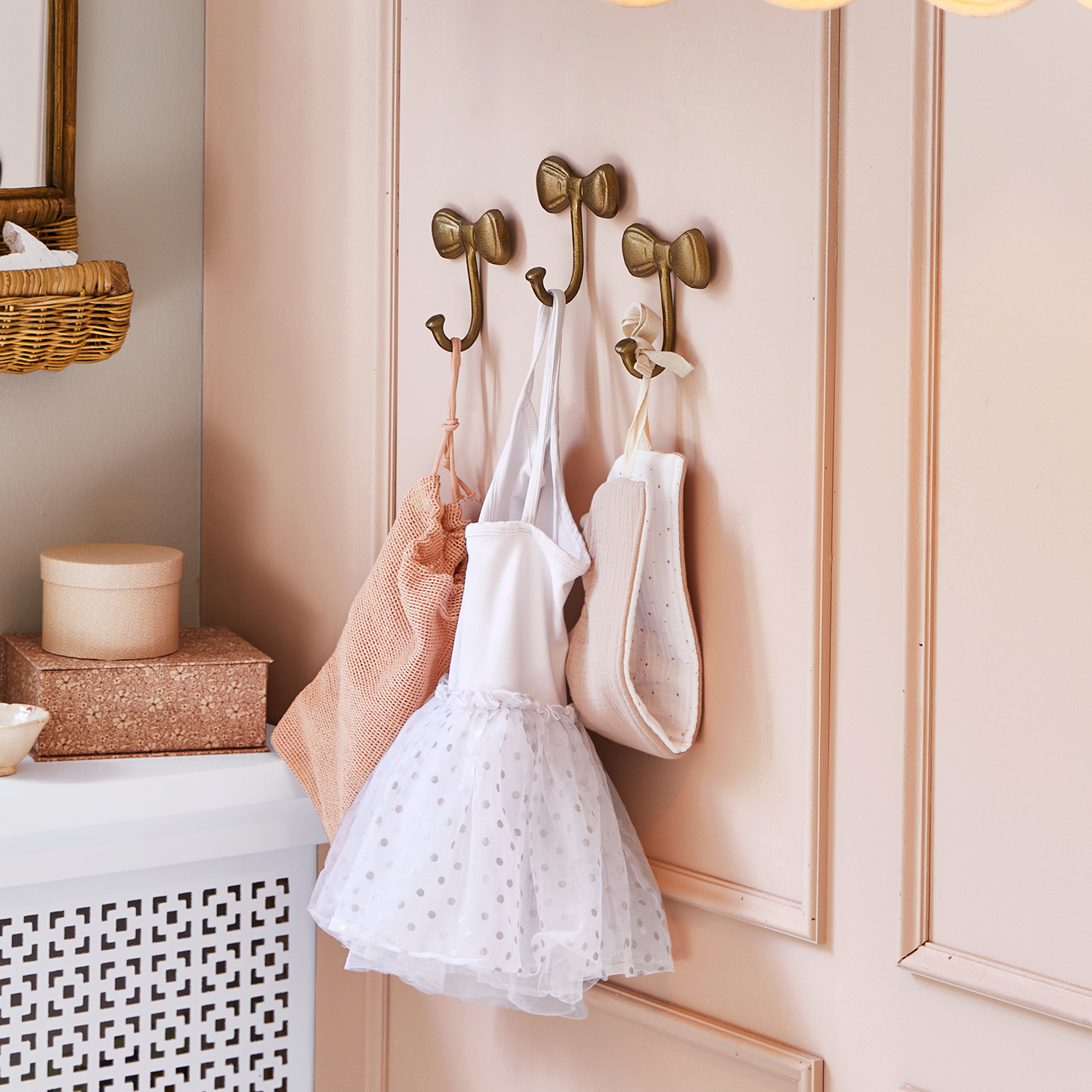 Ganci metallici dorati a forma di fiocco su parete rosa con abbigliamento per bambini appeso
