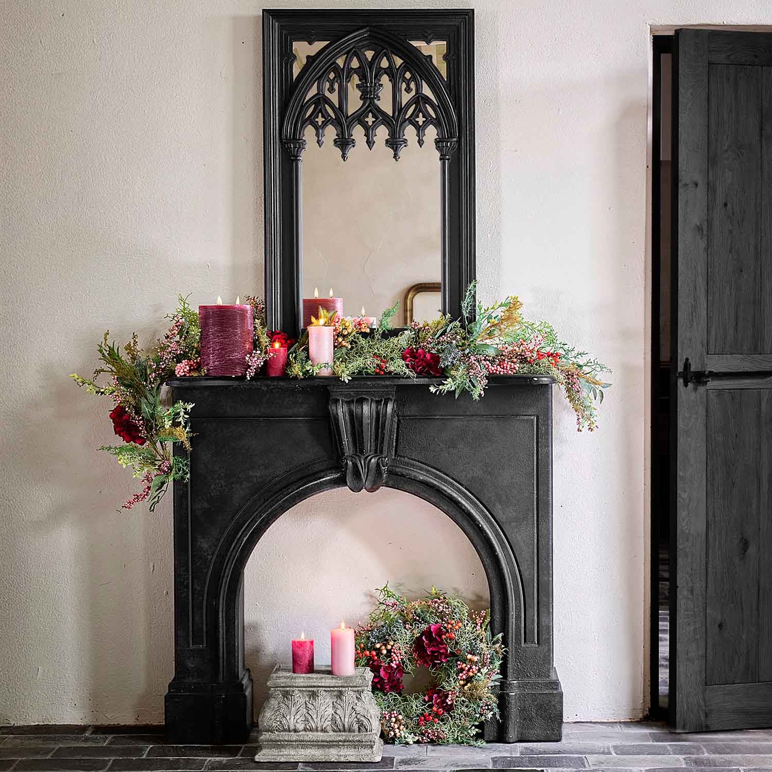 Camino nero decorativo con specchio gotico, decorato con candele rosse e ghirlande verdi per interni