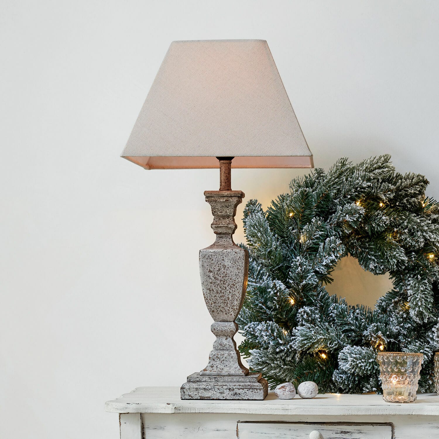 Lampada da tavolo Gorham Lampada da tavolo in pietra beige con paralume accanto a corona natalizia verde con luci decorative