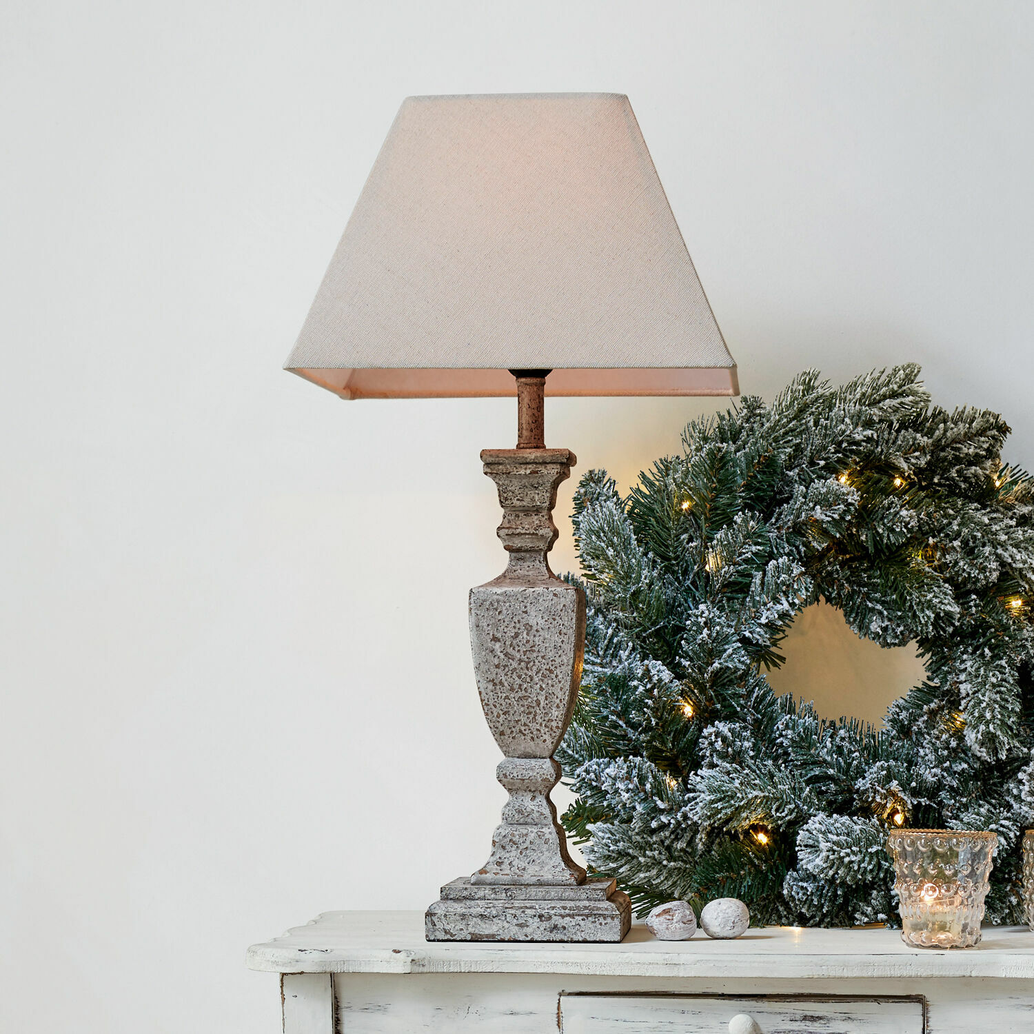 Lampada da tavolo Gorham Lampada da tavolo in pietra beige con paralume accanto a corona natalizia verde con luci decorative