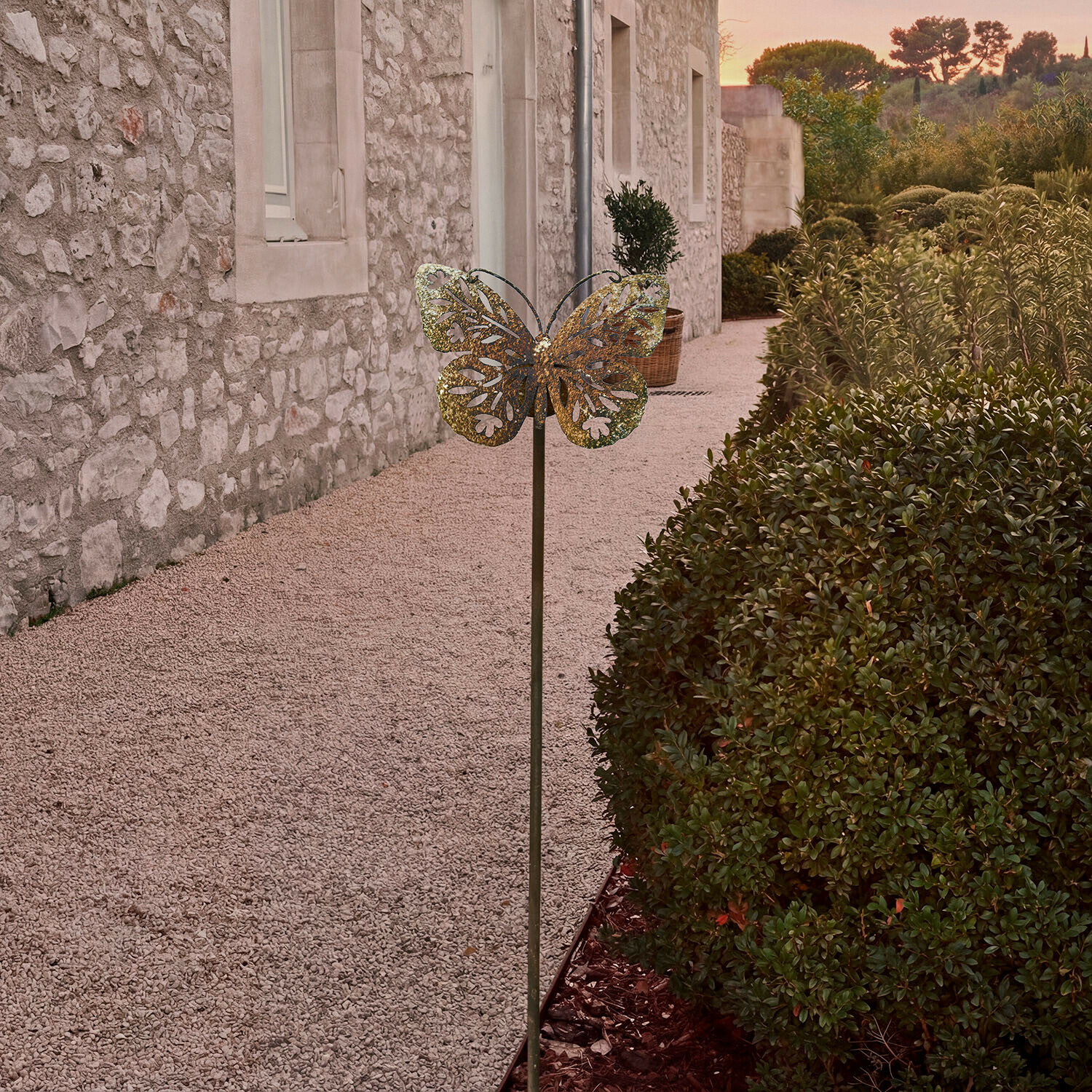 Bastone da giardino Jélomiane Decorazione da giardino in metallo a forma di farfalla color ottone davanti a muro in pietra e cespugli verdi