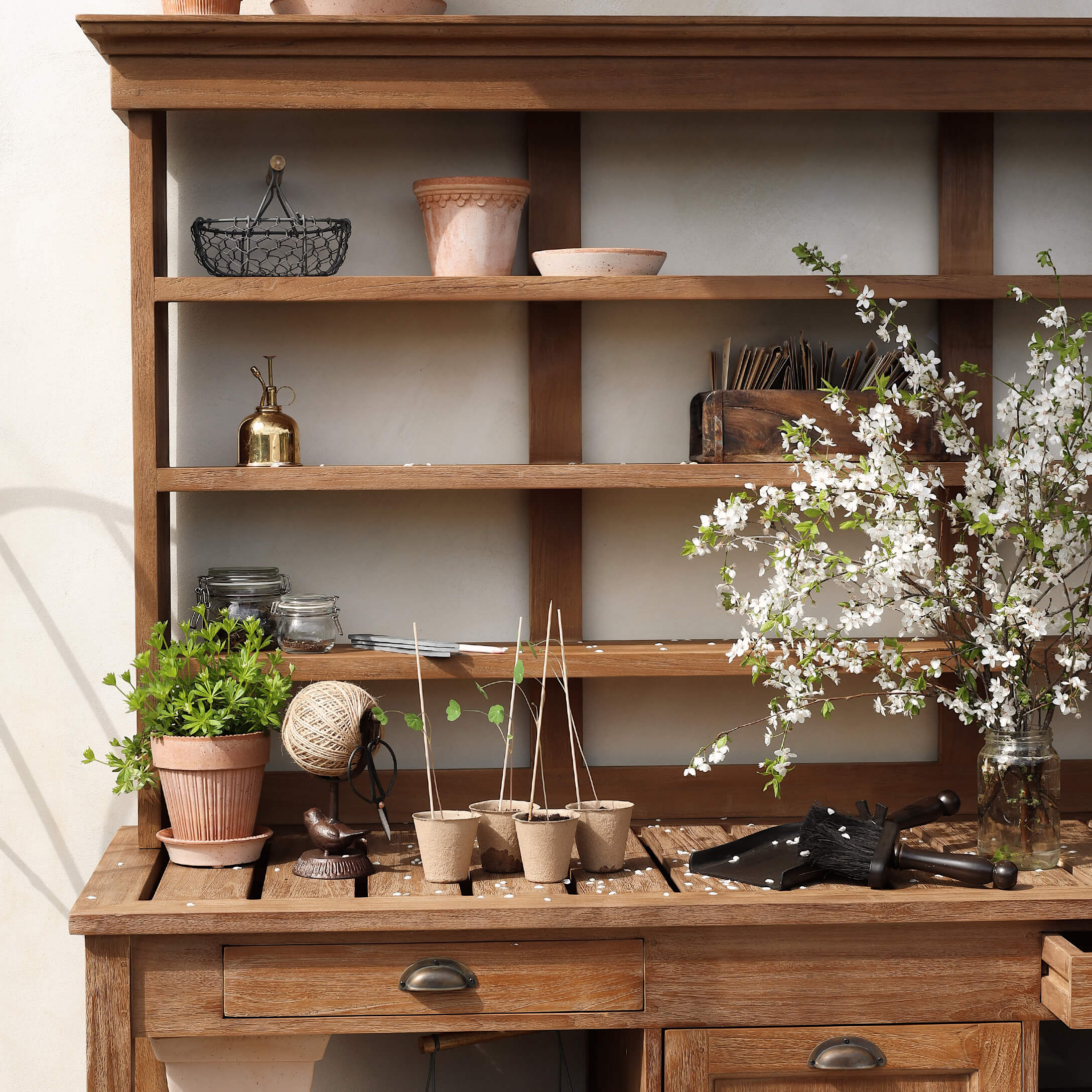 Tavolo da giardino in legno con vasi, attrezzi da giardinaggio e rami fioriti in vaso di vetro