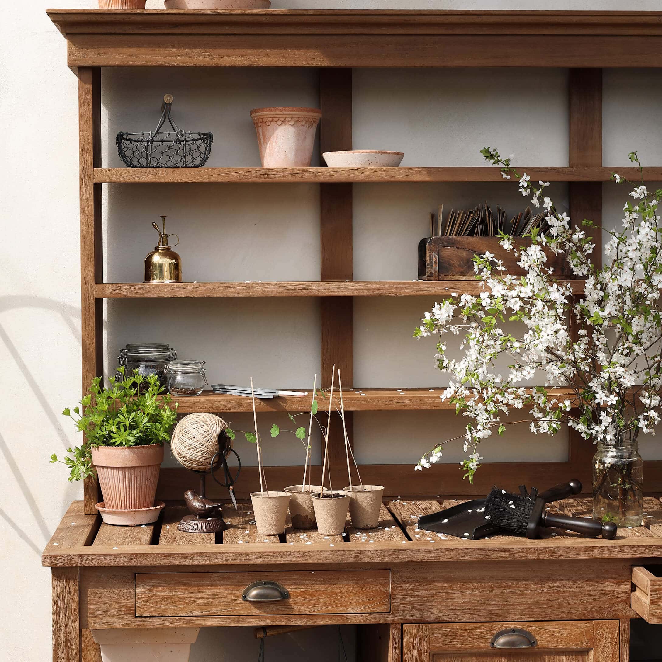 Tavolo da giardino in legno con vasi, attrezzi da giardinaggio e rami fioriti in vaso di vetro