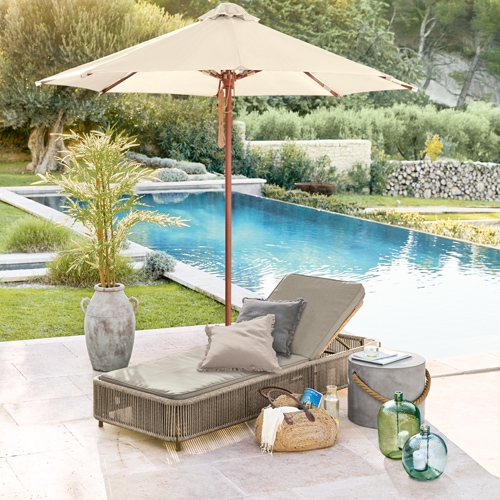Lettino da giardino beige con cuscini e ombrellone vicino alla piscina, decorazioni in rattan e vetro