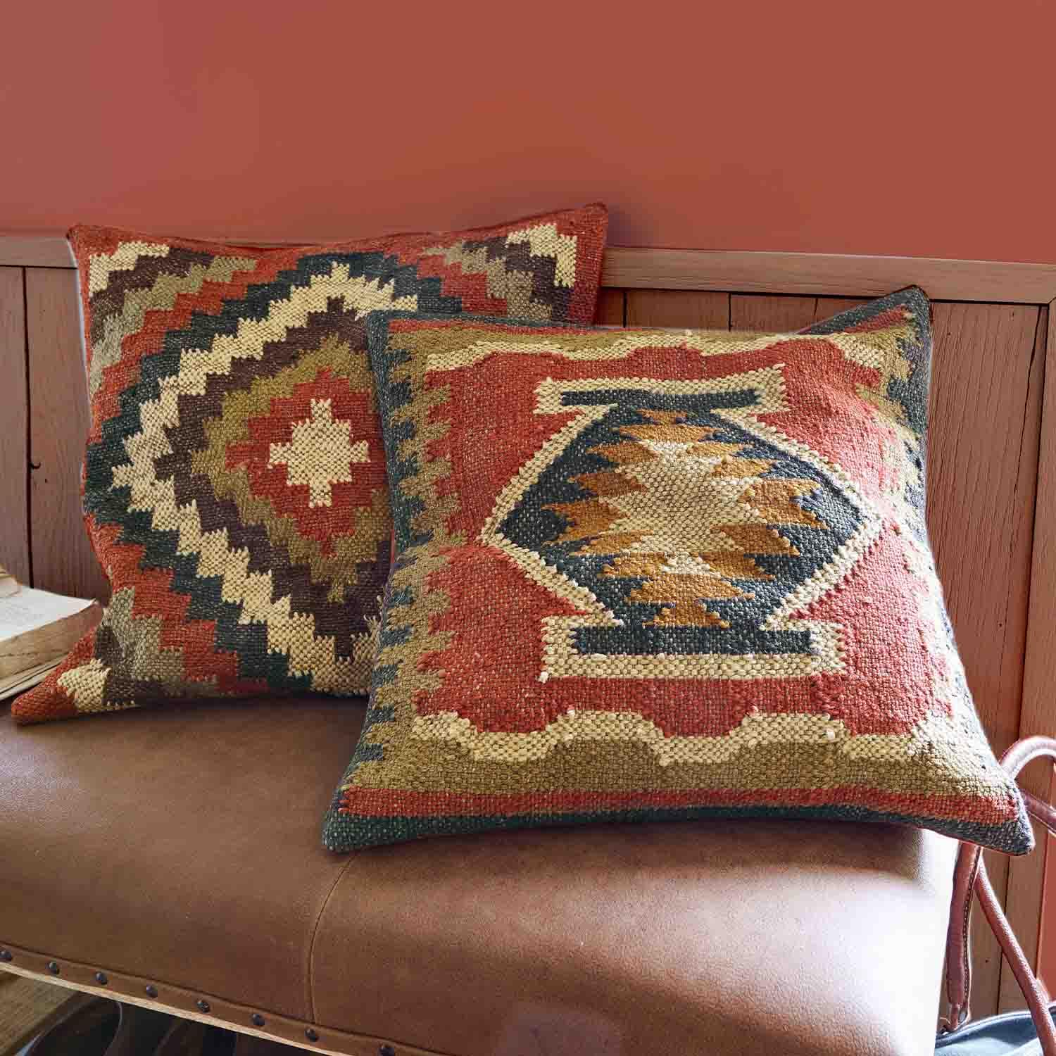 Due cuscini decorativi in tessuto con motivi geometrici in tonalità calde di rosso e beige su divano in pelle