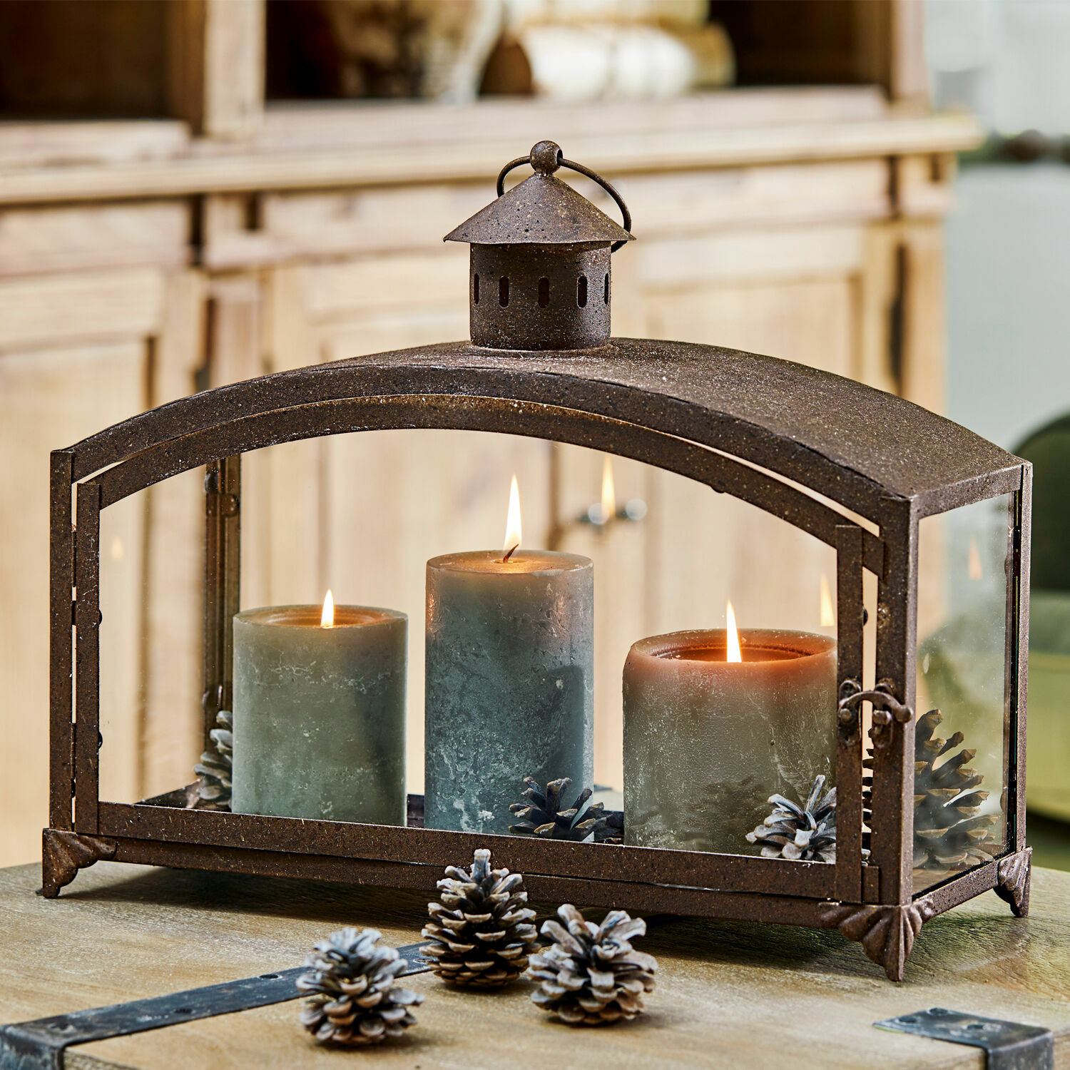 Lanterna Miora Lanterna in metallo con tre candele verdi e pigne su tavolo in legno, decorazione d'interni