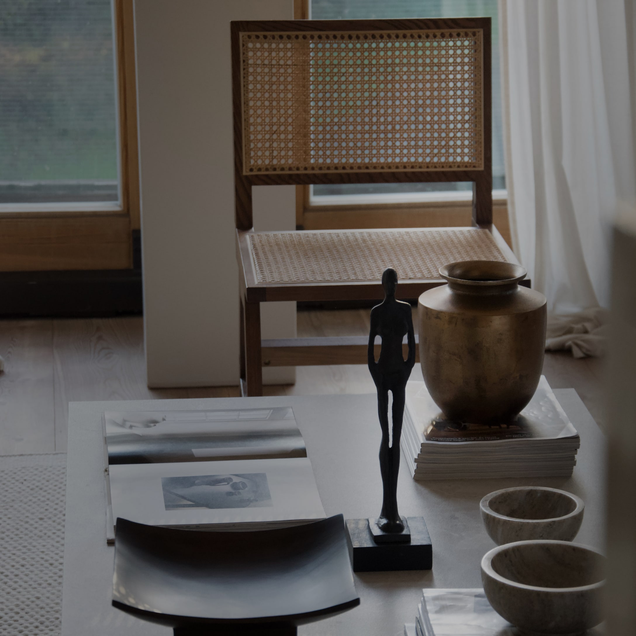 Tavolino decorativo con statua nera, vaso in ottone e sedia in rattan sullo sfondo