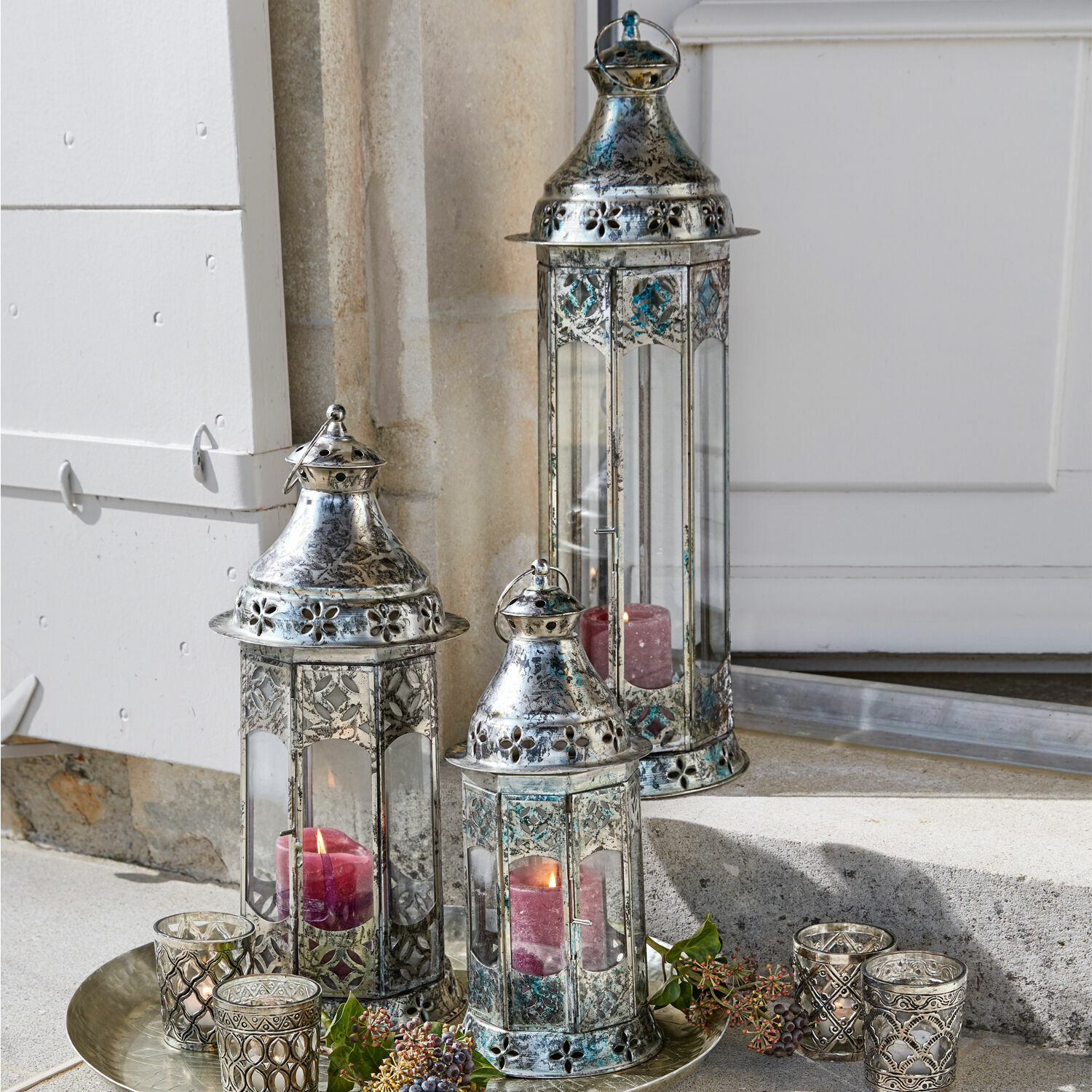 Set di 3 lanterne Aylin Set di tre lanterne in metallo argentato con candele rosse e decorazioni su un vassoio