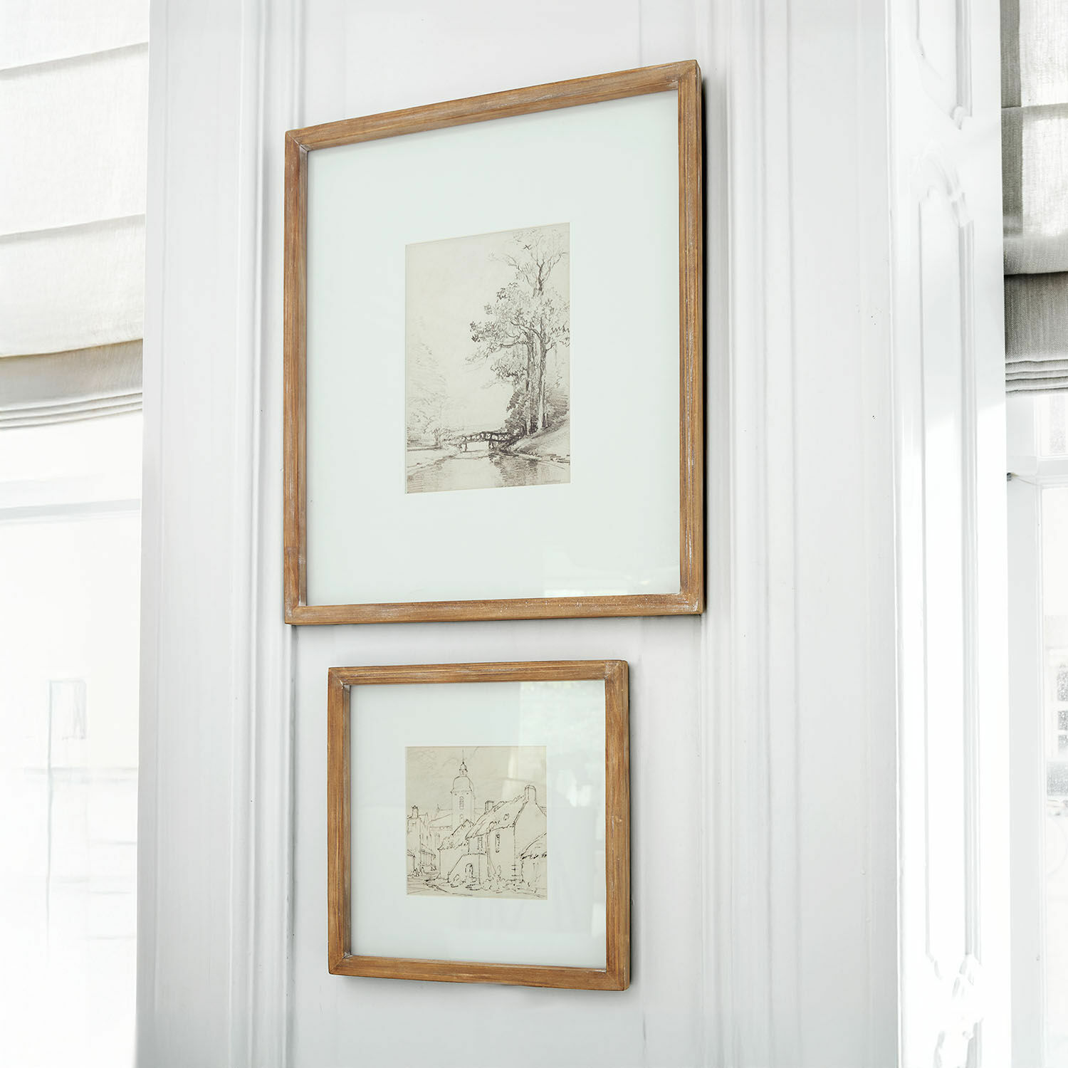 Coppia di quadri Juvarel Due cornici rustiche in legno con disegni di paesaggi appese a parete bianca luminosa