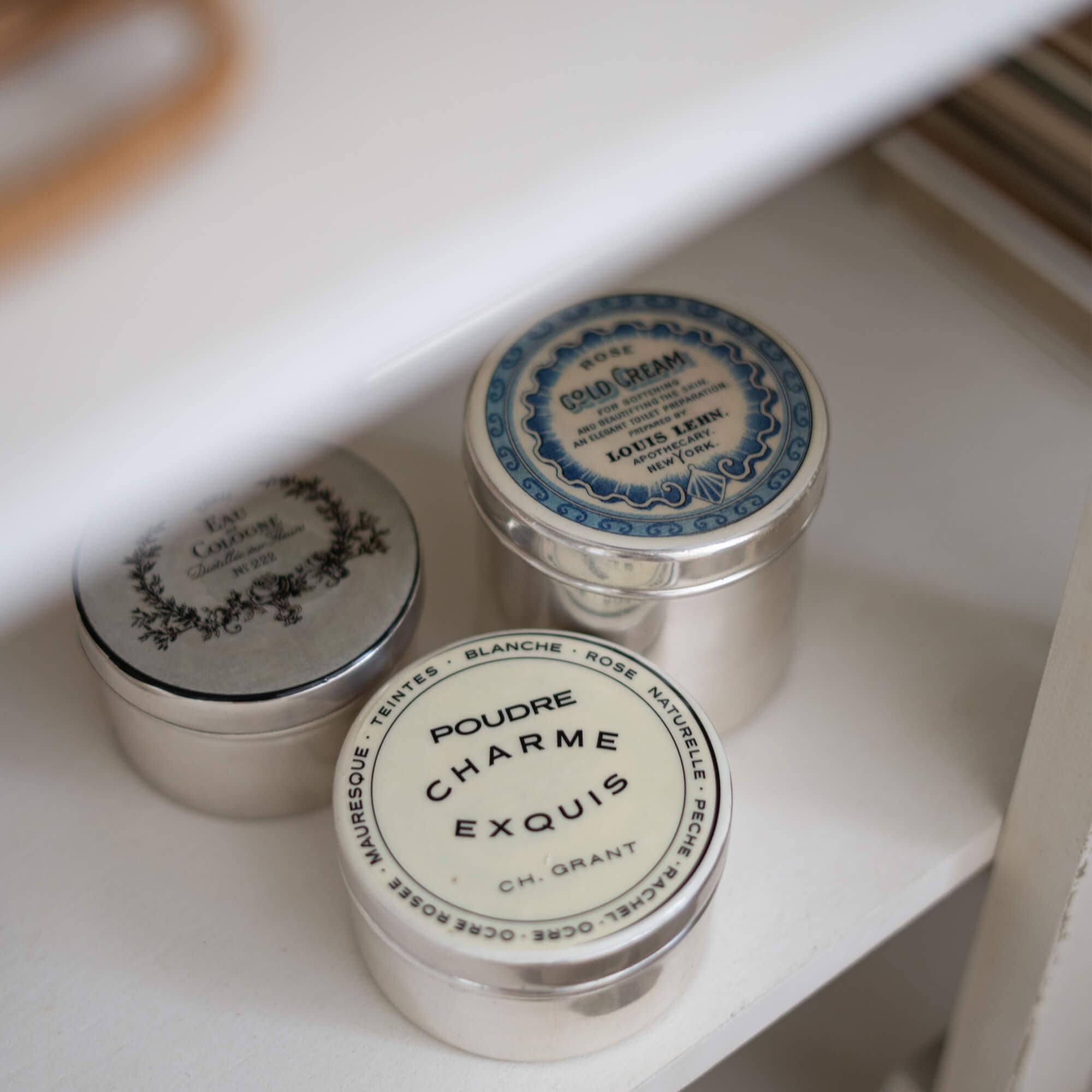 Tre barattoli metallici vintage per cosmetici su mensola bianca per conservazione