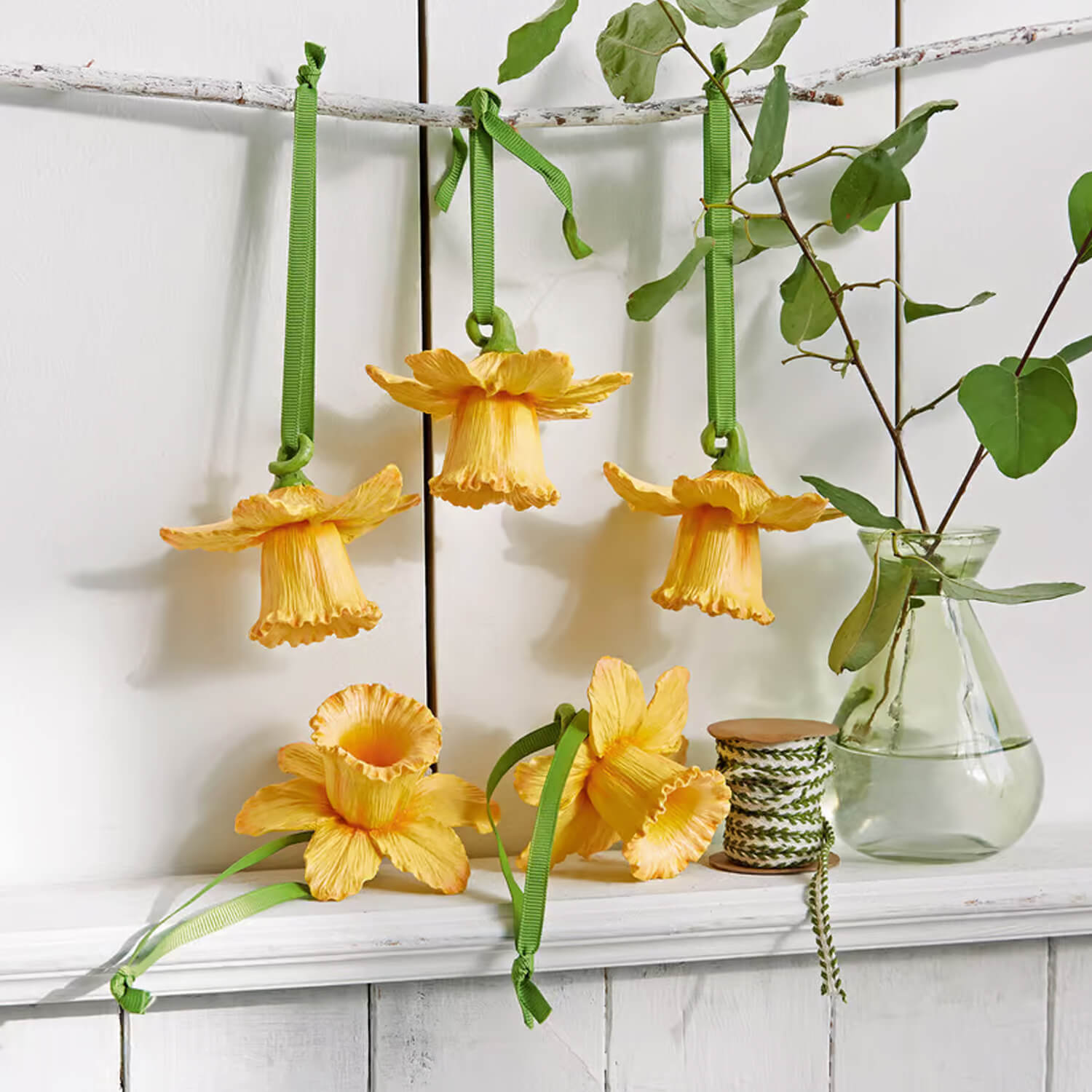 Decorazioni floreali gialle con nastri verdi appese su mensola bianca, decorazione primaverile