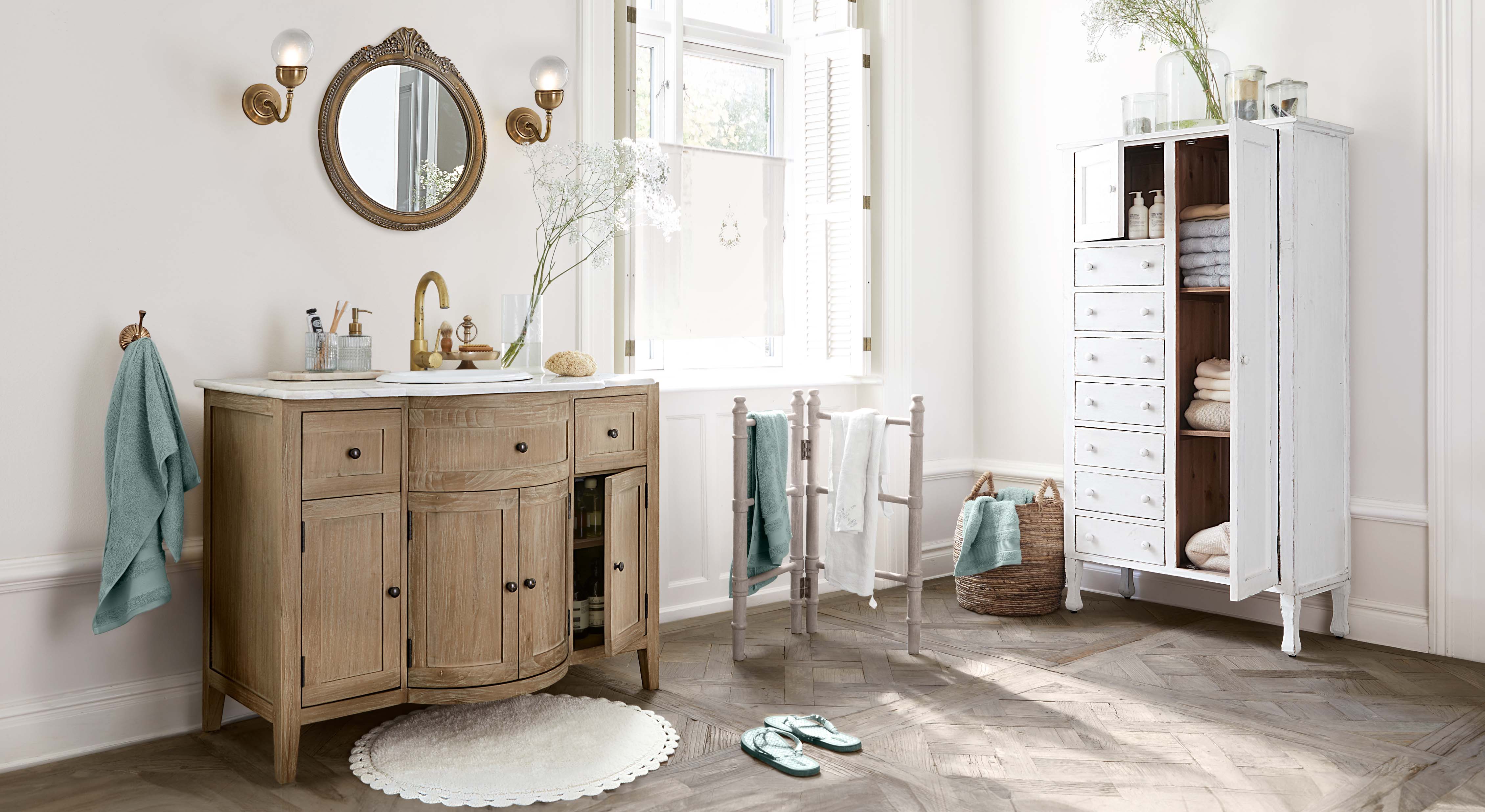 Bagno con mobile lavabo in legno, armadio bianco e asciugamani turchesi, ambiente luminoso e naturale