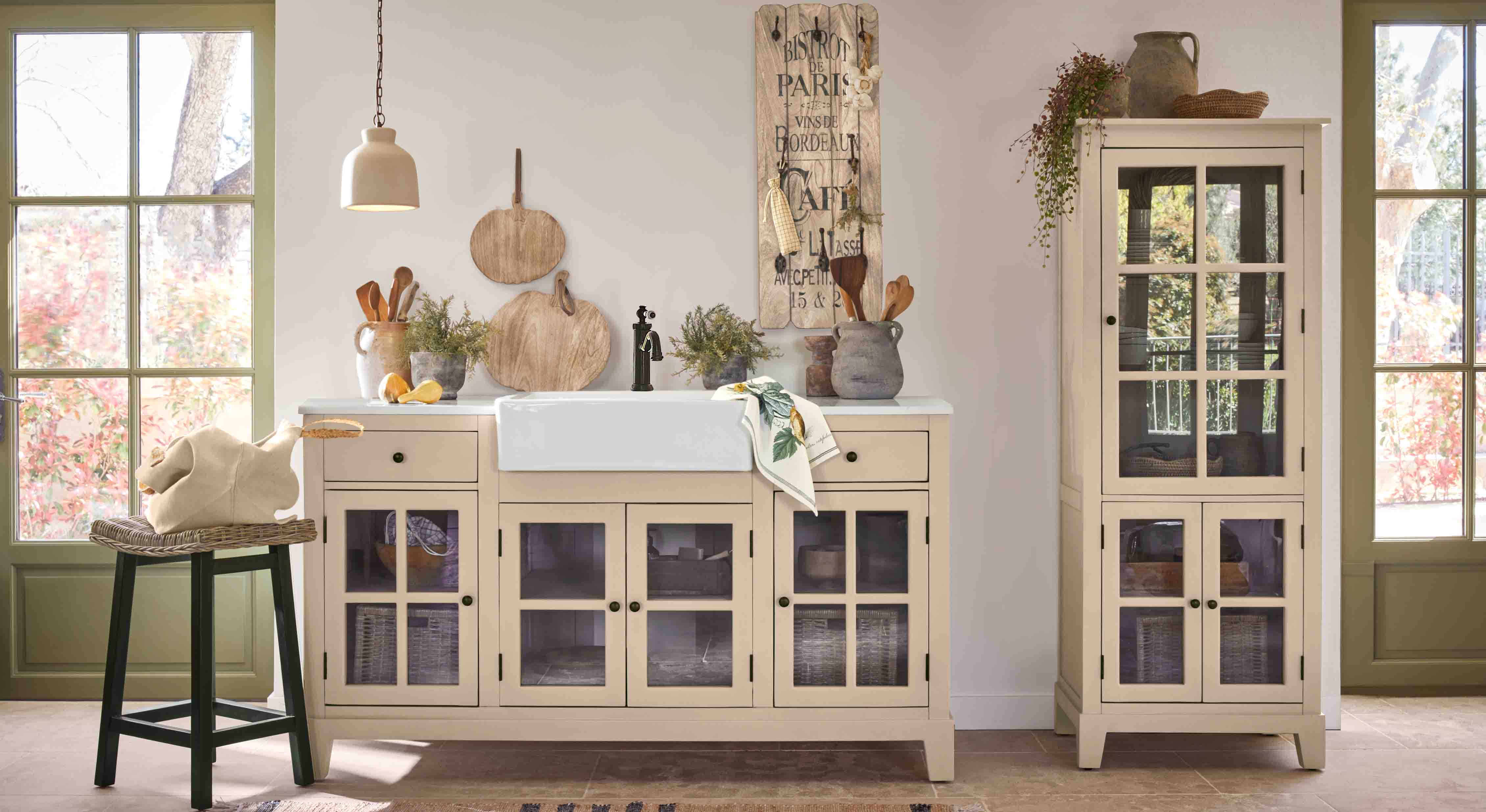 Cucina rustica con mobili beige a vetro e lavello in ceramica bianca, decorazioni in legno e piante