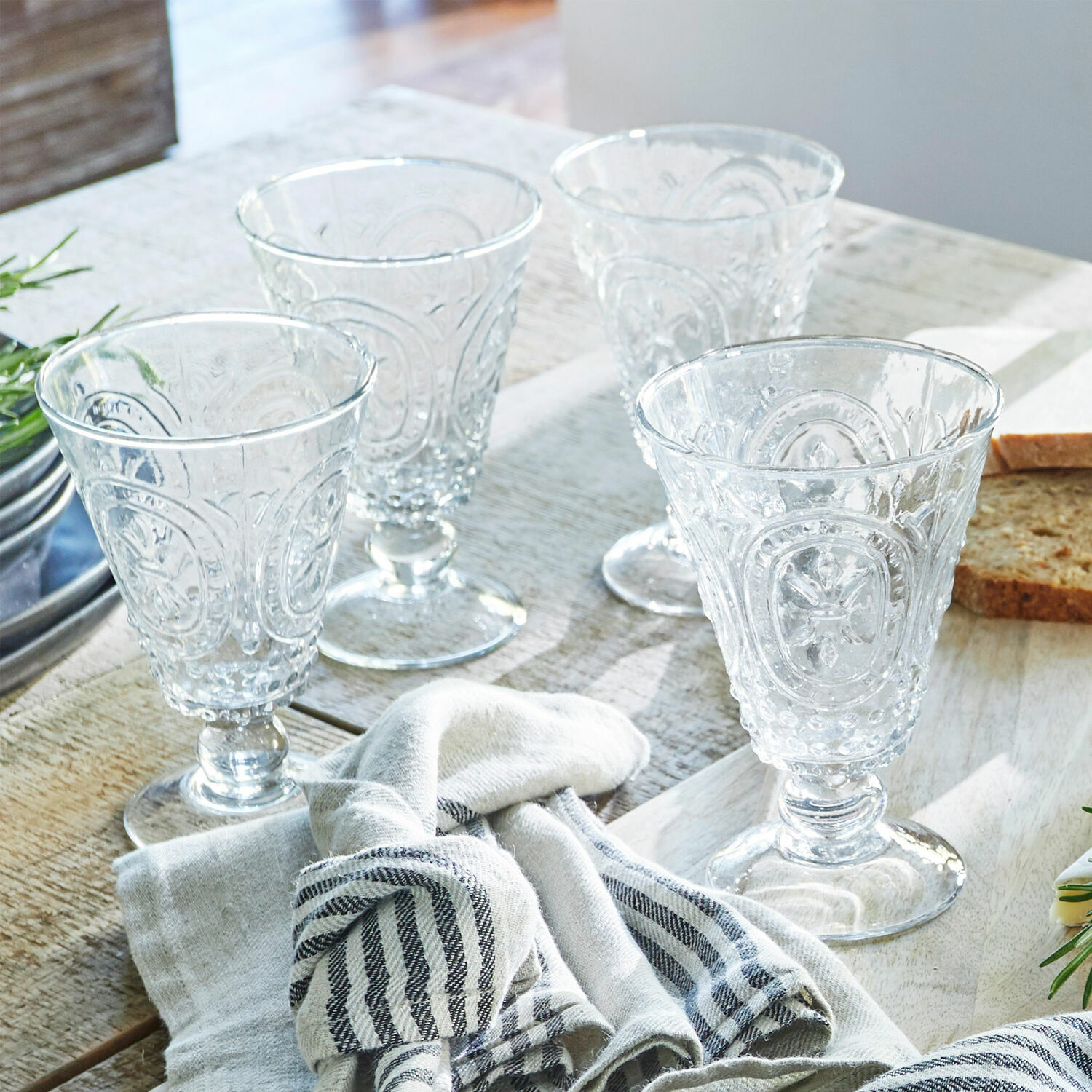 Set di 4 bicchieri da vino Sarton Set di quattro bicchieri trasparenti con motivo decorativo su tavolo in legno con tessuto e pane