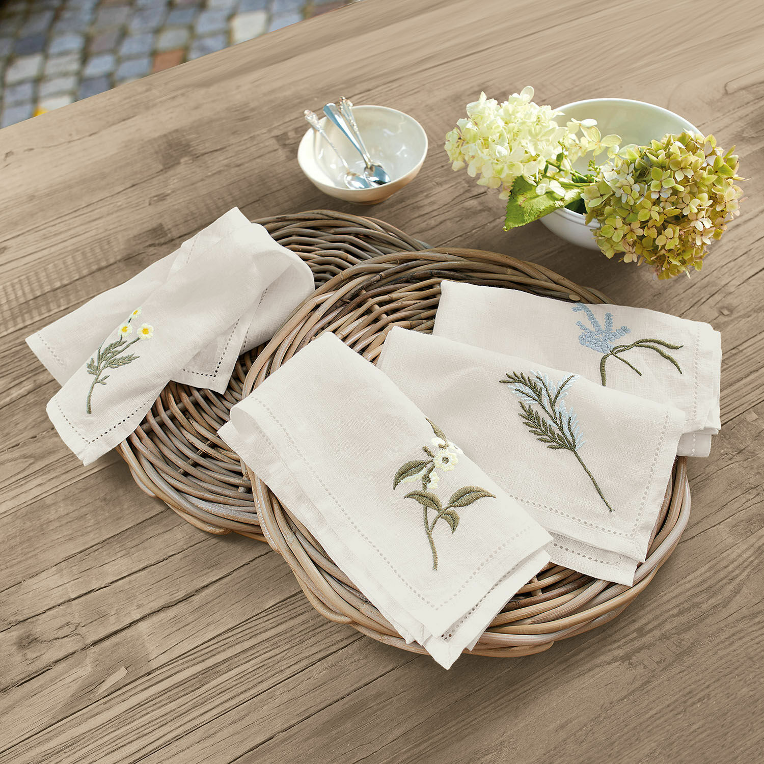 Set di 4 tovaglioli Lentilly Tovaglioli di lino naturale con ricamo floreale su cesto di vimini su tavolo in legno