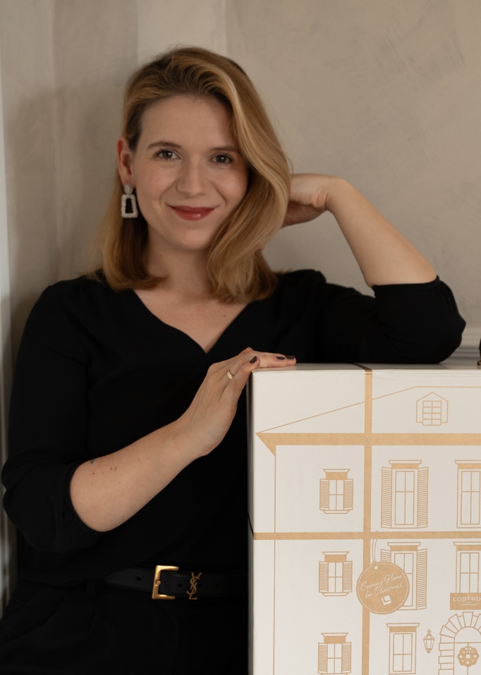 Donna con maglia nera che tiene una scatola bianca con disegno di casa, decorazione natalizia