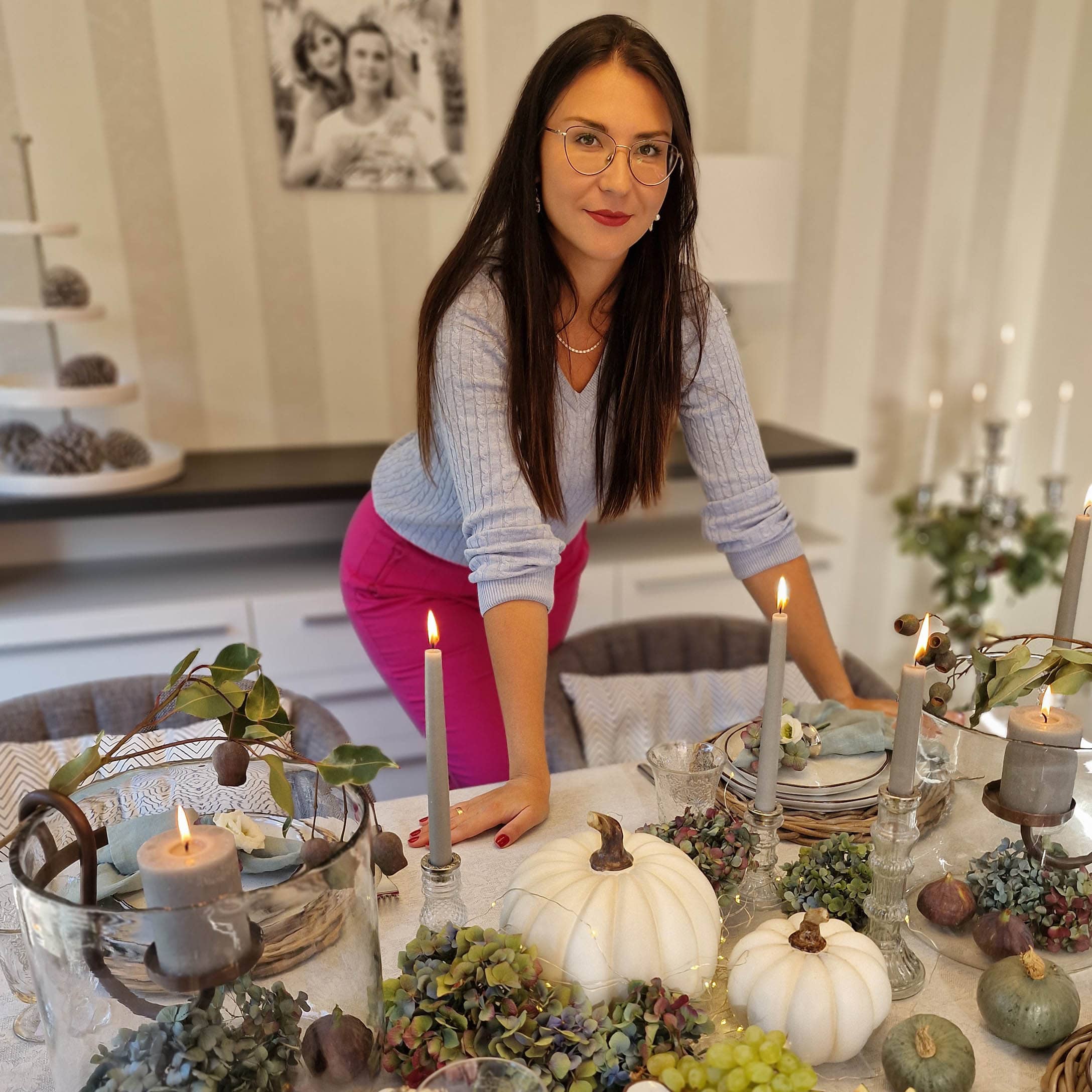 Donna vicino a tavolo con decorazioni autunnali di zucche bianche, candele e fiori verdi in casa