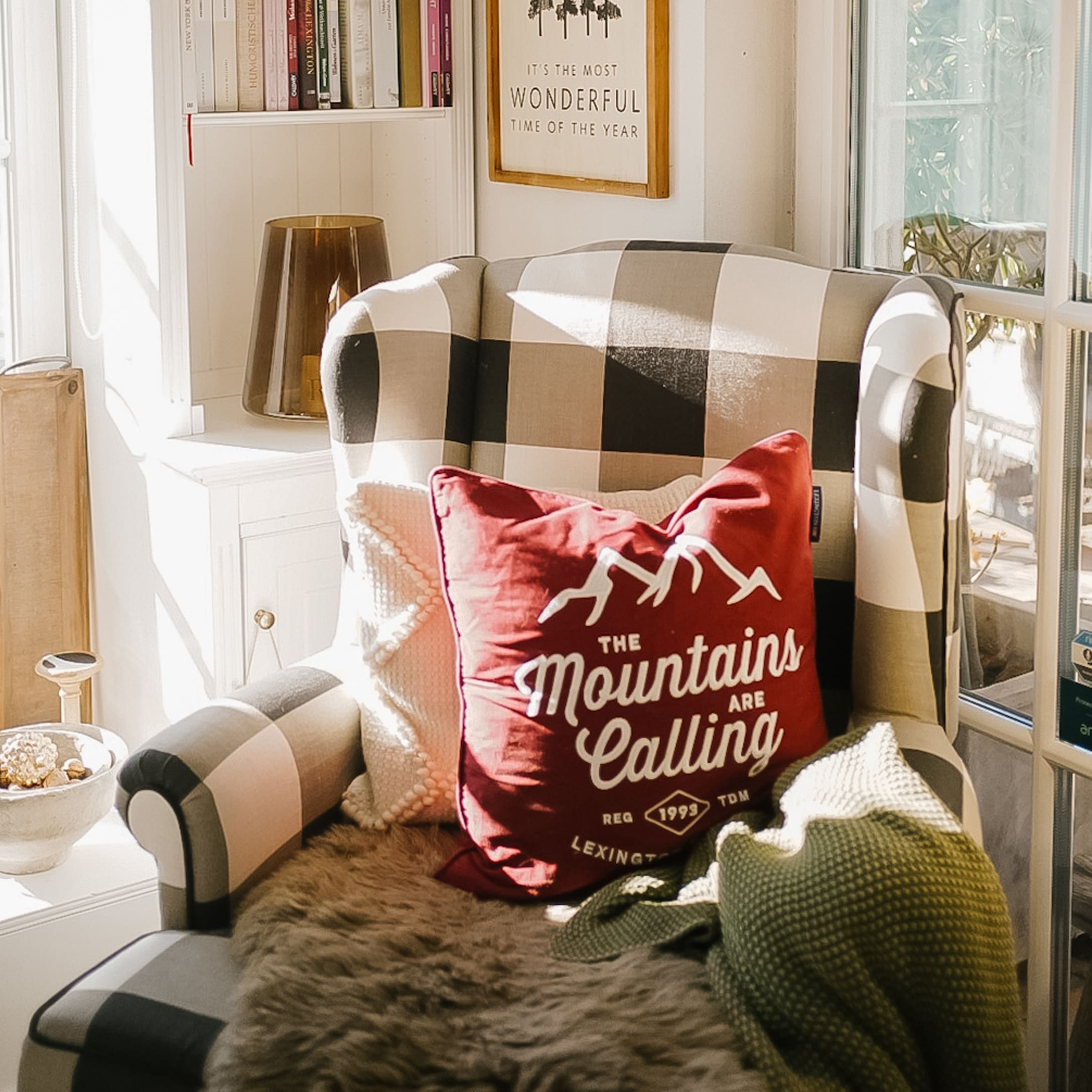 Poltrona a quadri con cuscino rosso Mountains e coperta morbida in ambiente luminoso