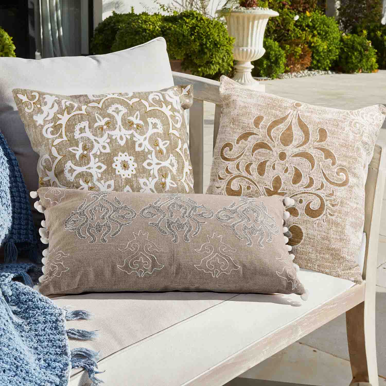 Set di tre cuscini decorativi beige e bianchi con motivi su divano chiaro all'aperto