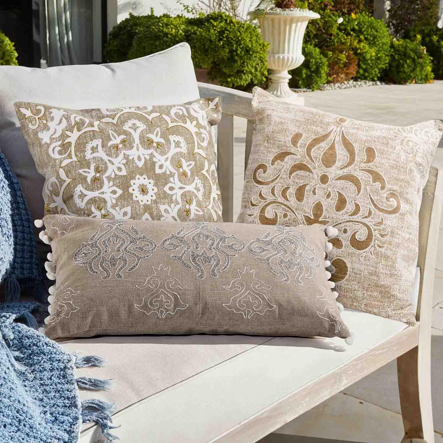 Set di tre cuscini decorativi beige e bianchi con motivi su divano chiaro all'aperto