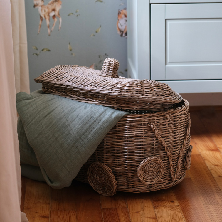 Cesto in vimini a forma di auto con coperta verde su pavimento in legno in camera dei bambini