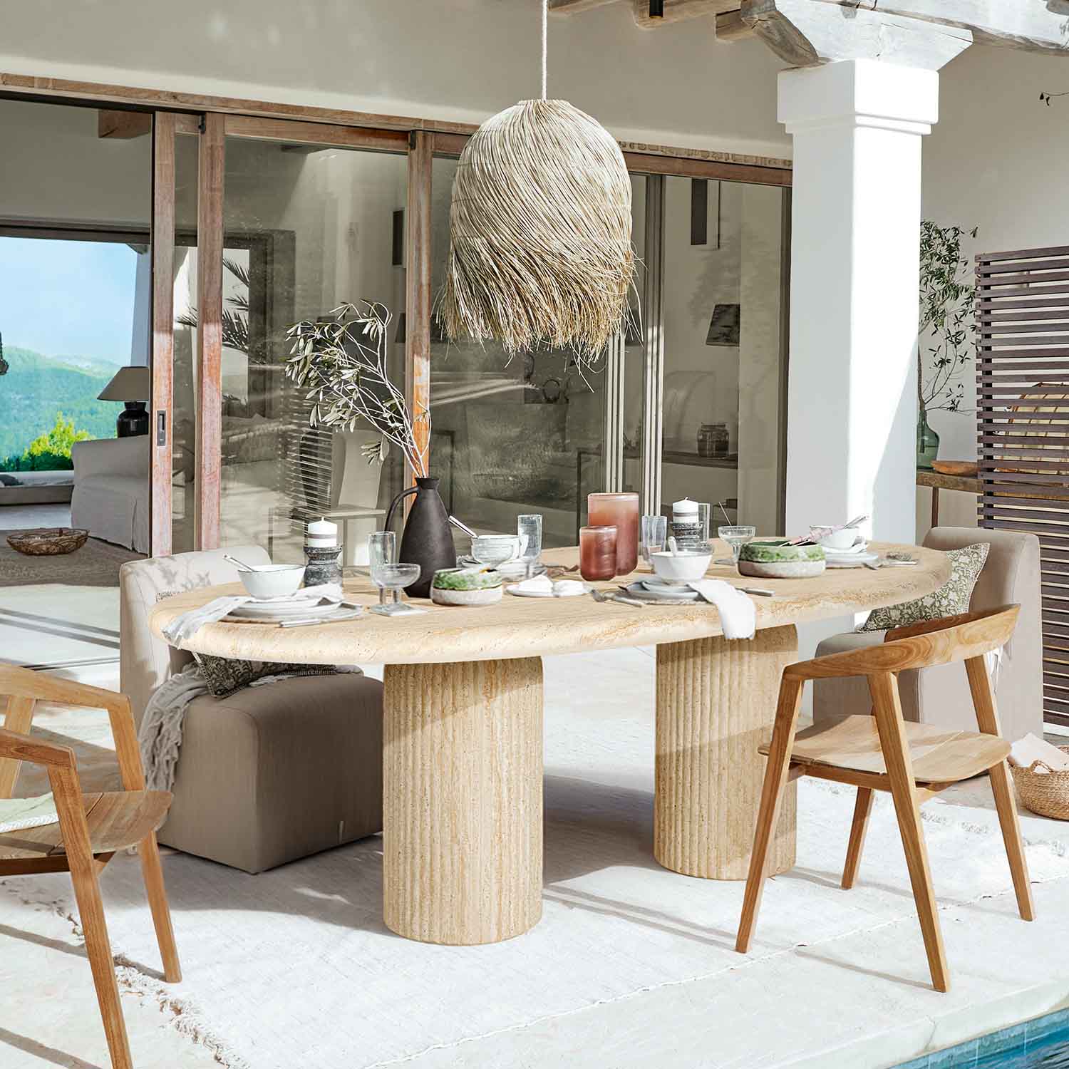 Tavolo da pranzo in pietra chiara con gambe cilindriche, circondato da sedie in legno e imbottite in ambiente luminoso