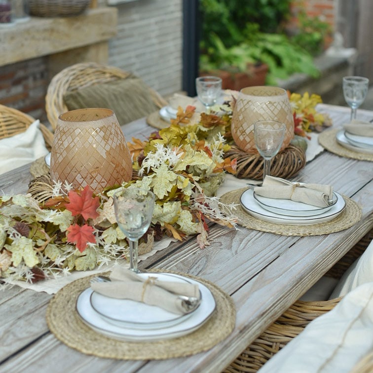Tavolo rustico in legno decorato con foglie naturali e lanterne in rattan per un'atmosfera accogliente