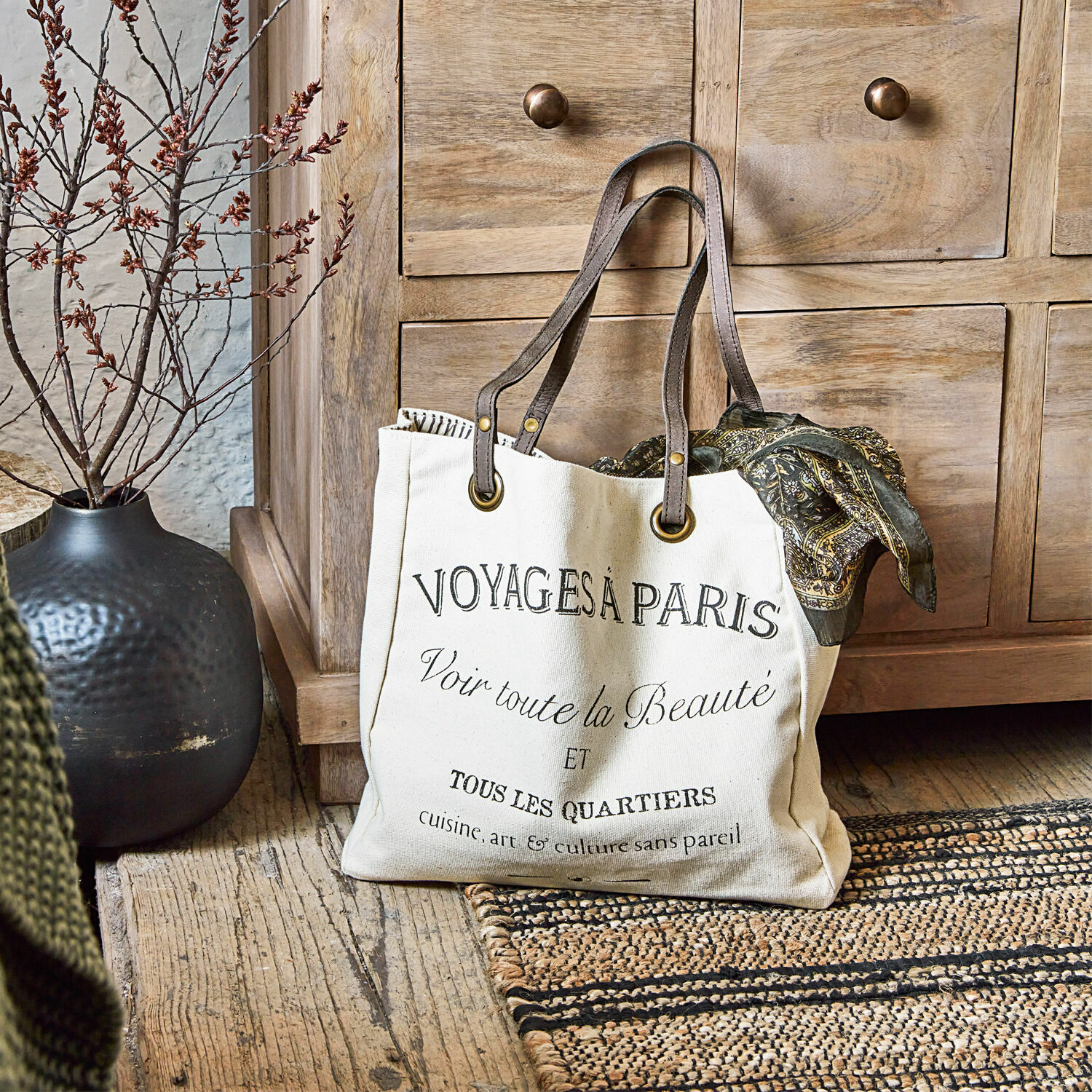 Borsa Voyage Borsa in cotone beige con stampa nera e manici marroni su pavimento in legno