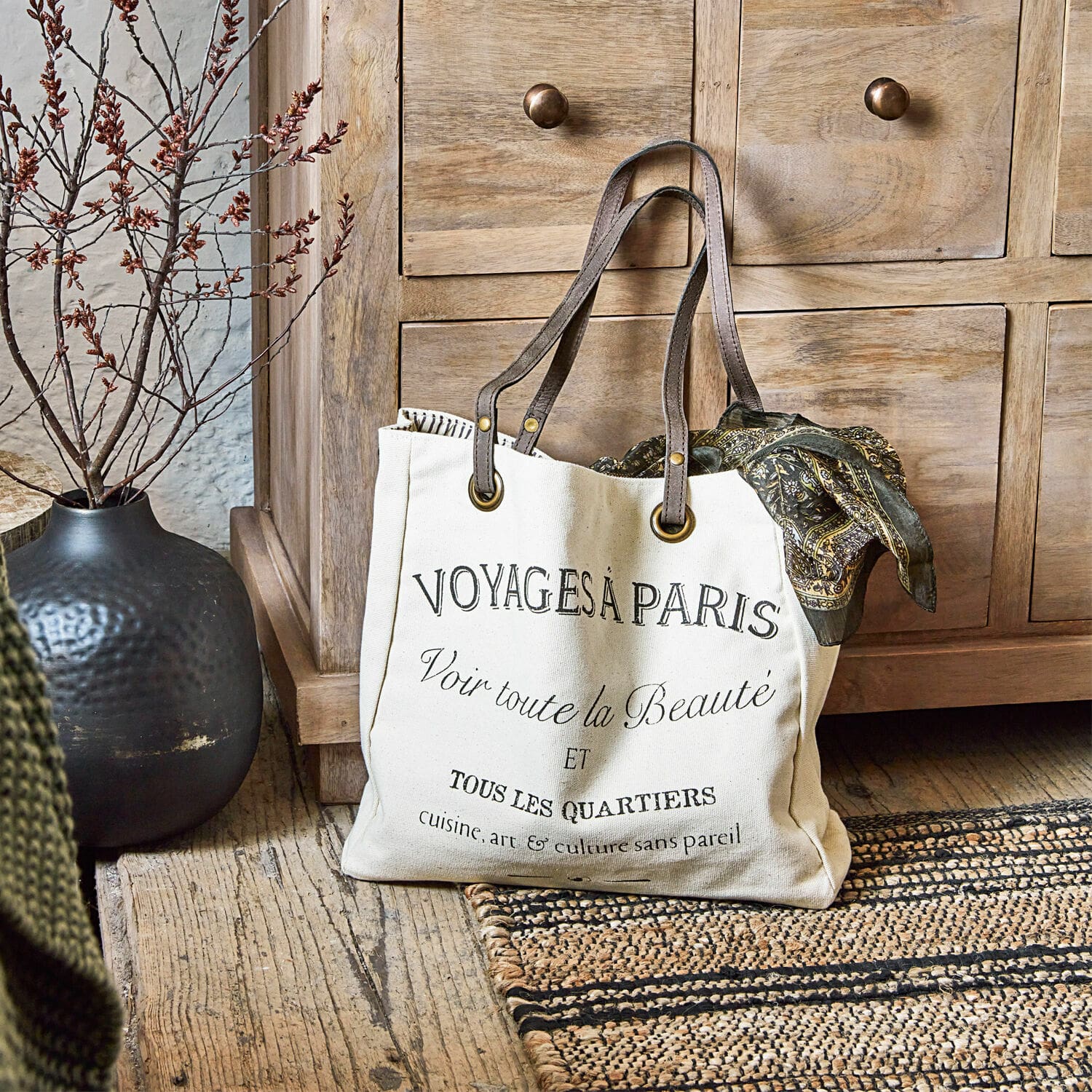 Borsa Voyage Borsa in cotone beige con stampa nera e manici marroni su pavimento in legno