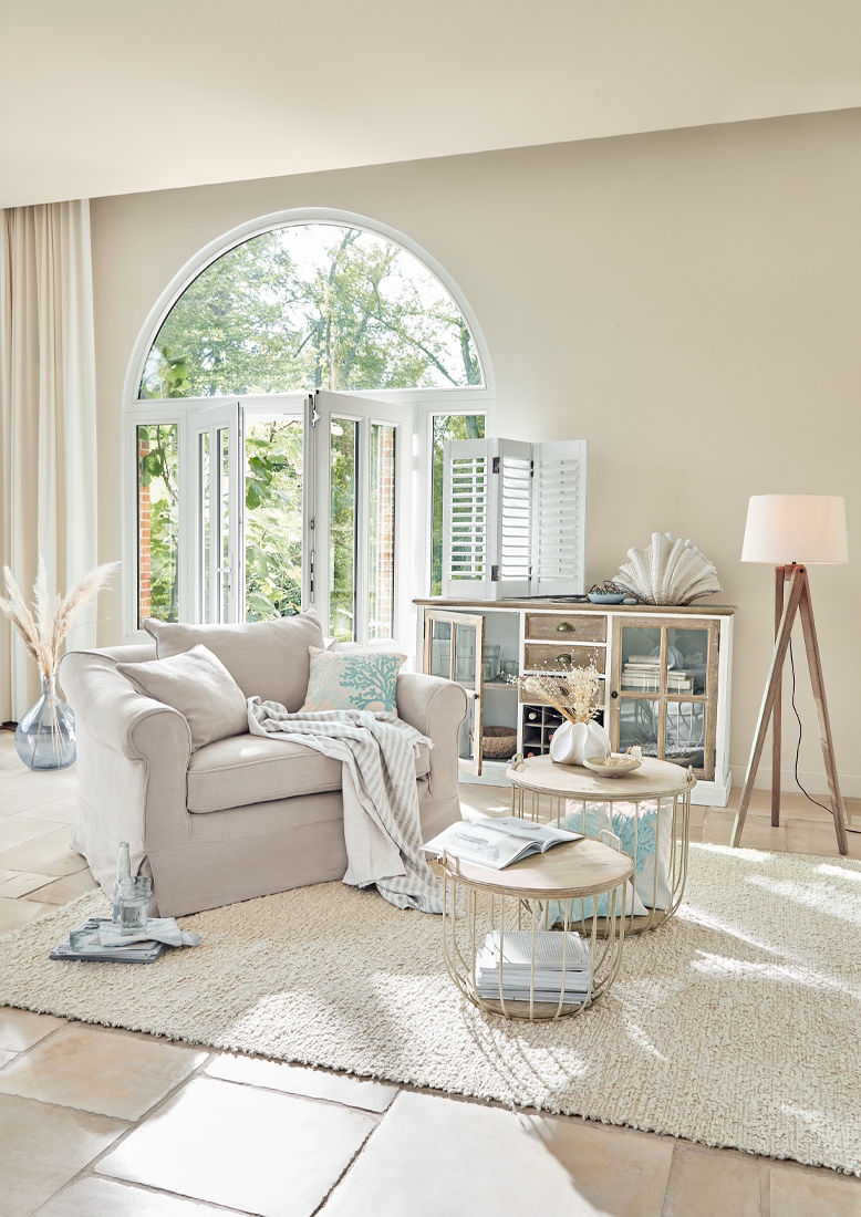 Comoda poltrona beige con cuscino e coperta in soggiorno luminoso con finestra e lampada da terra
