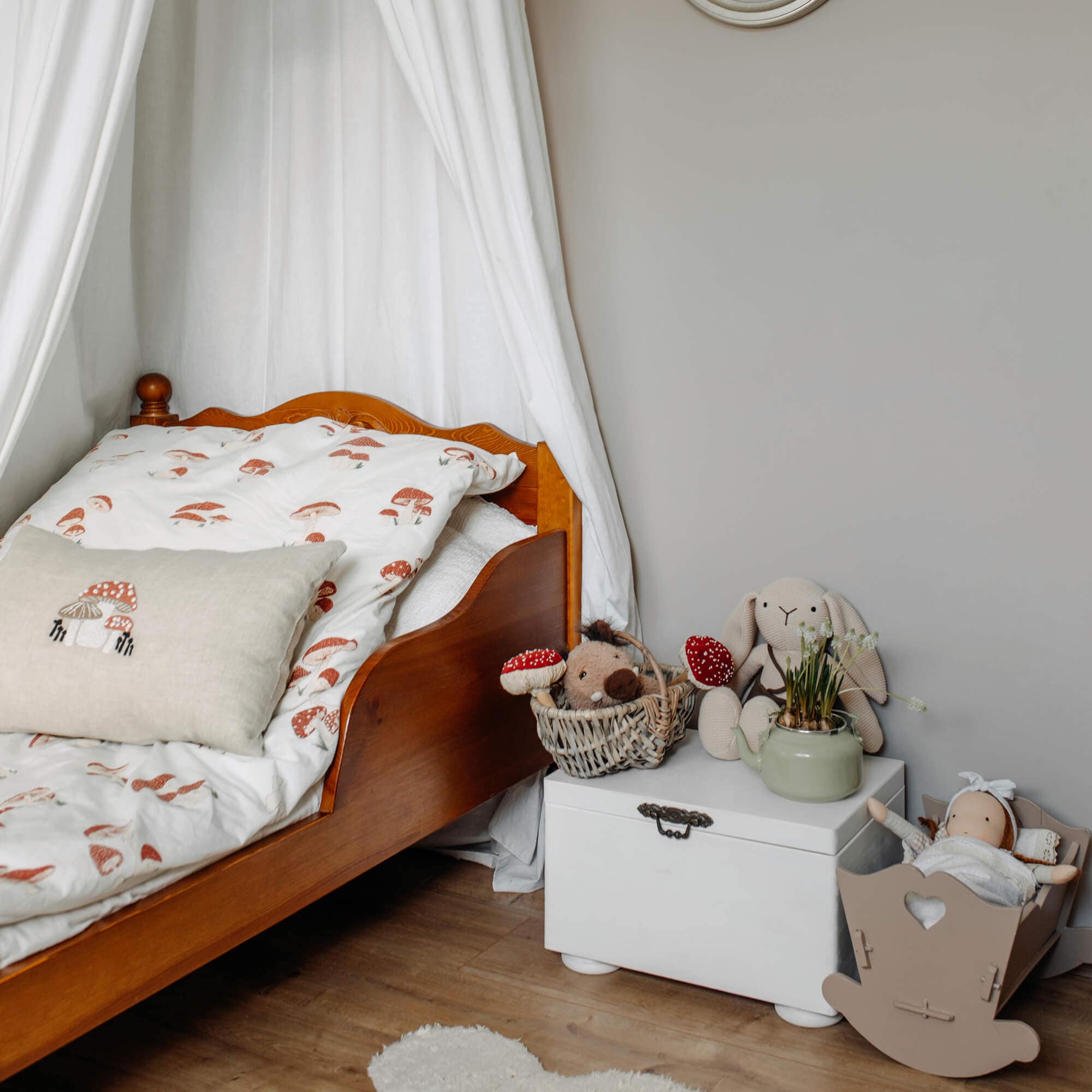 Letto in legno per bambini con biancheria da letto bianca a funghi e peluche su cassapanca bianca