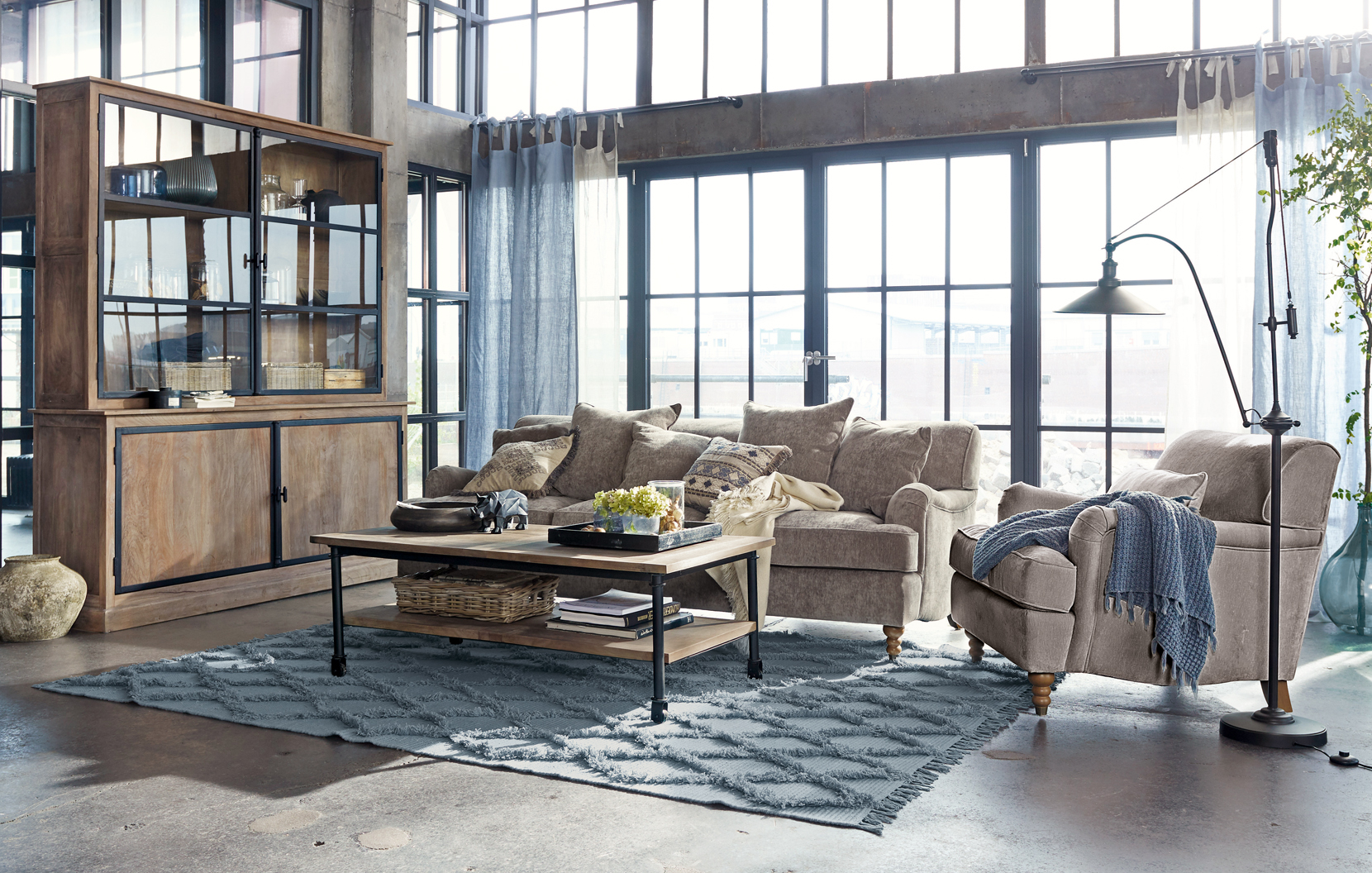 Accogliente soggiorno in stile loft con divano beige, mobile in legno e tappeto blu su pavimento in cemento